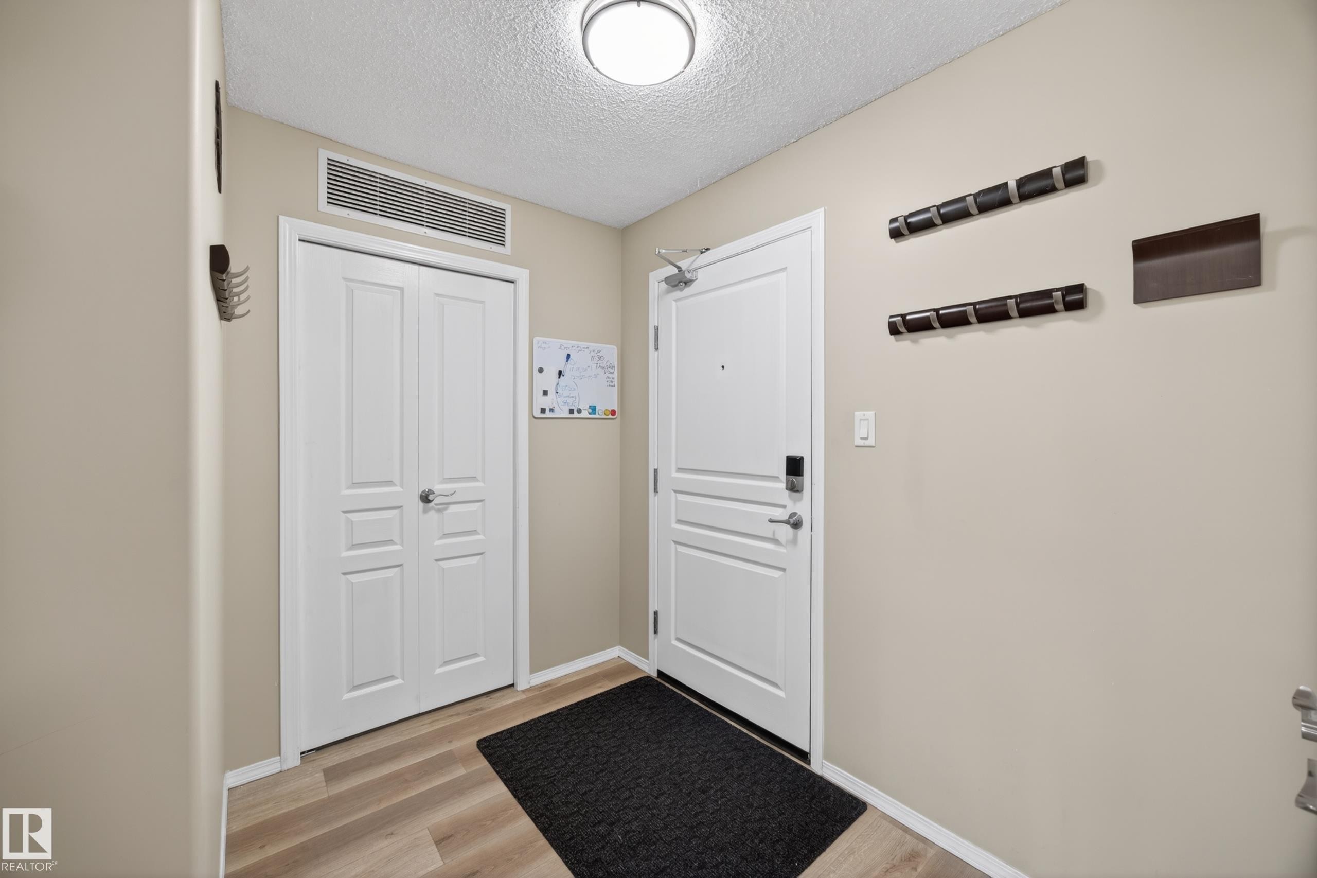 Entryway featuring wood-finish flooring, a white paneled door with smart lock, and a double-door closet with overhead ventilation - 138 16035 132 Street, Edmonton, AB