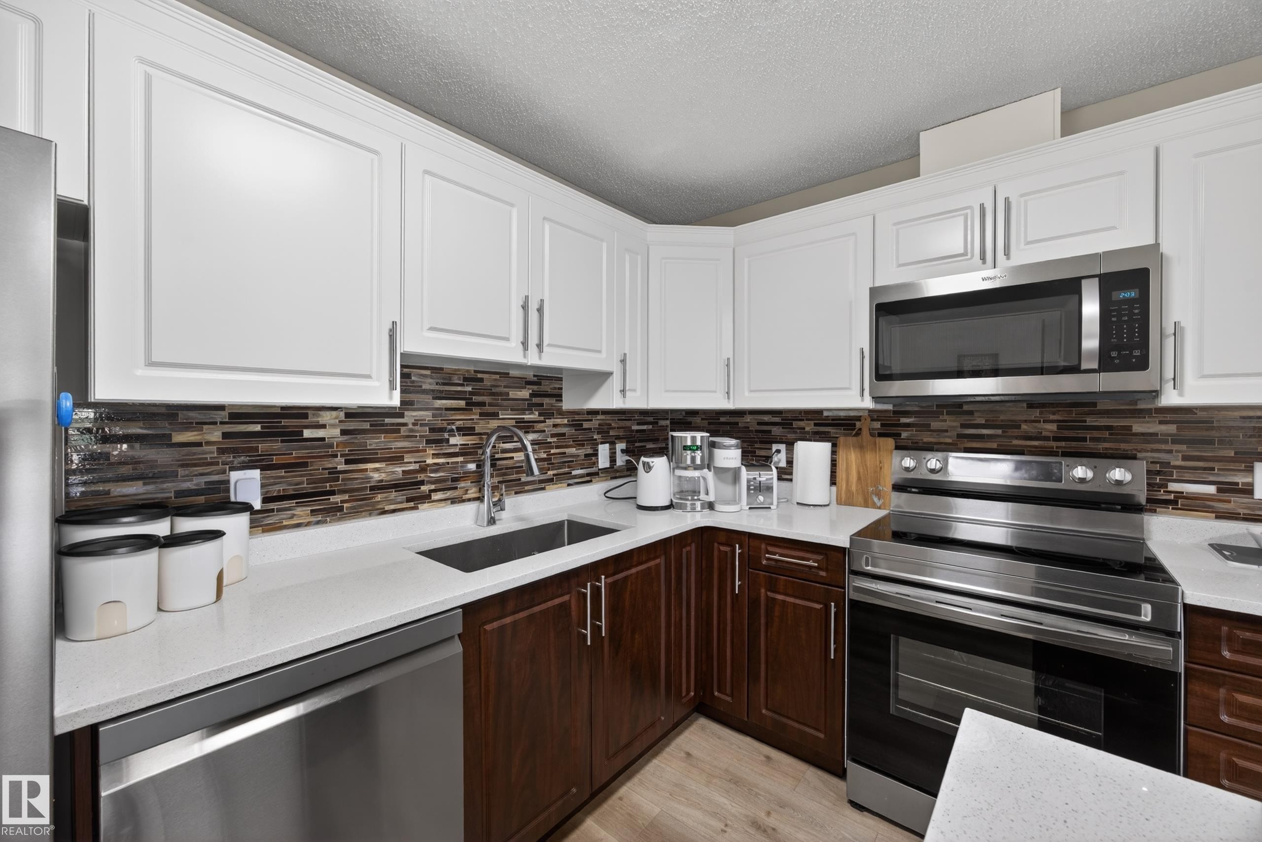Kitchen featuring white upper cabinetry, rich wood-finish lower cabinetry, and a mosaic tile backsplash - 138 16035 132 Street, Edmonton, AB