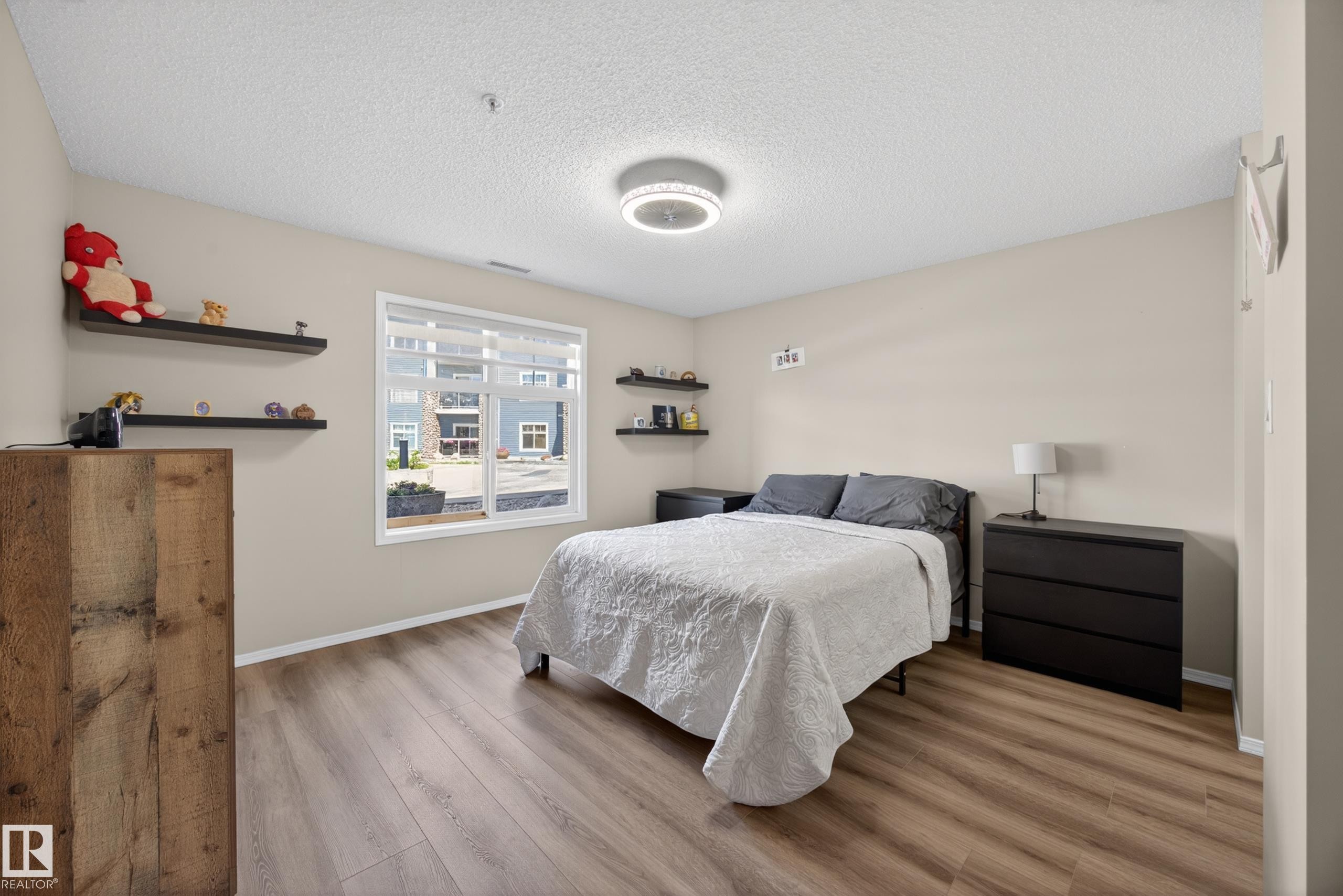 Spacious room featuring wood-finish flooring, light neutral wall tones, and a large window with white trim - 138 16035 132 Street, Edmonton, AB