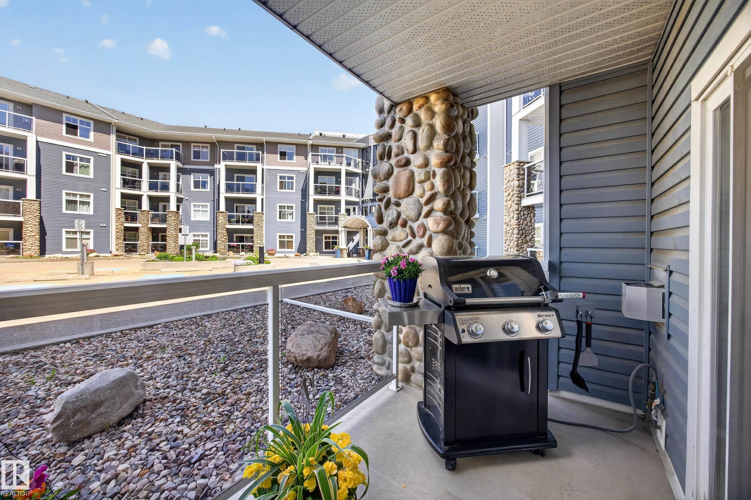 Covered patio featuring a concrete floor, stone-clad pillar, and gray horizontal siding - 138 16035 132 Street, Edmonton, AB