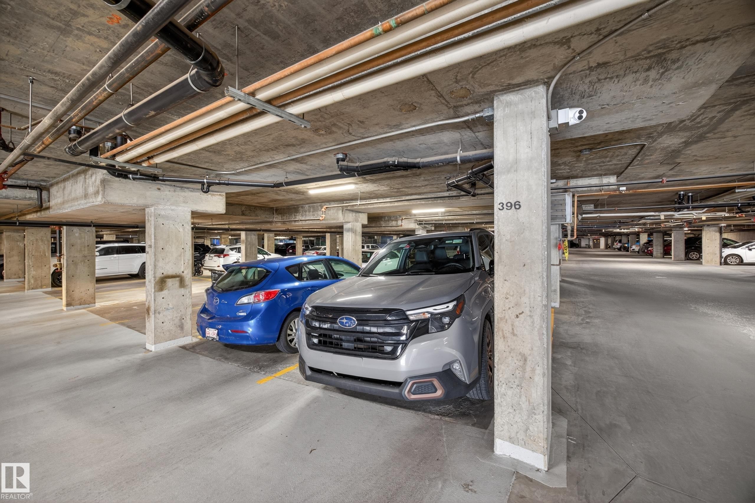 Dedicated parking space with concrete structural elements, exposed utility lines, and overhead lighting - 138 16035 132 Street, Edmonton, AB
