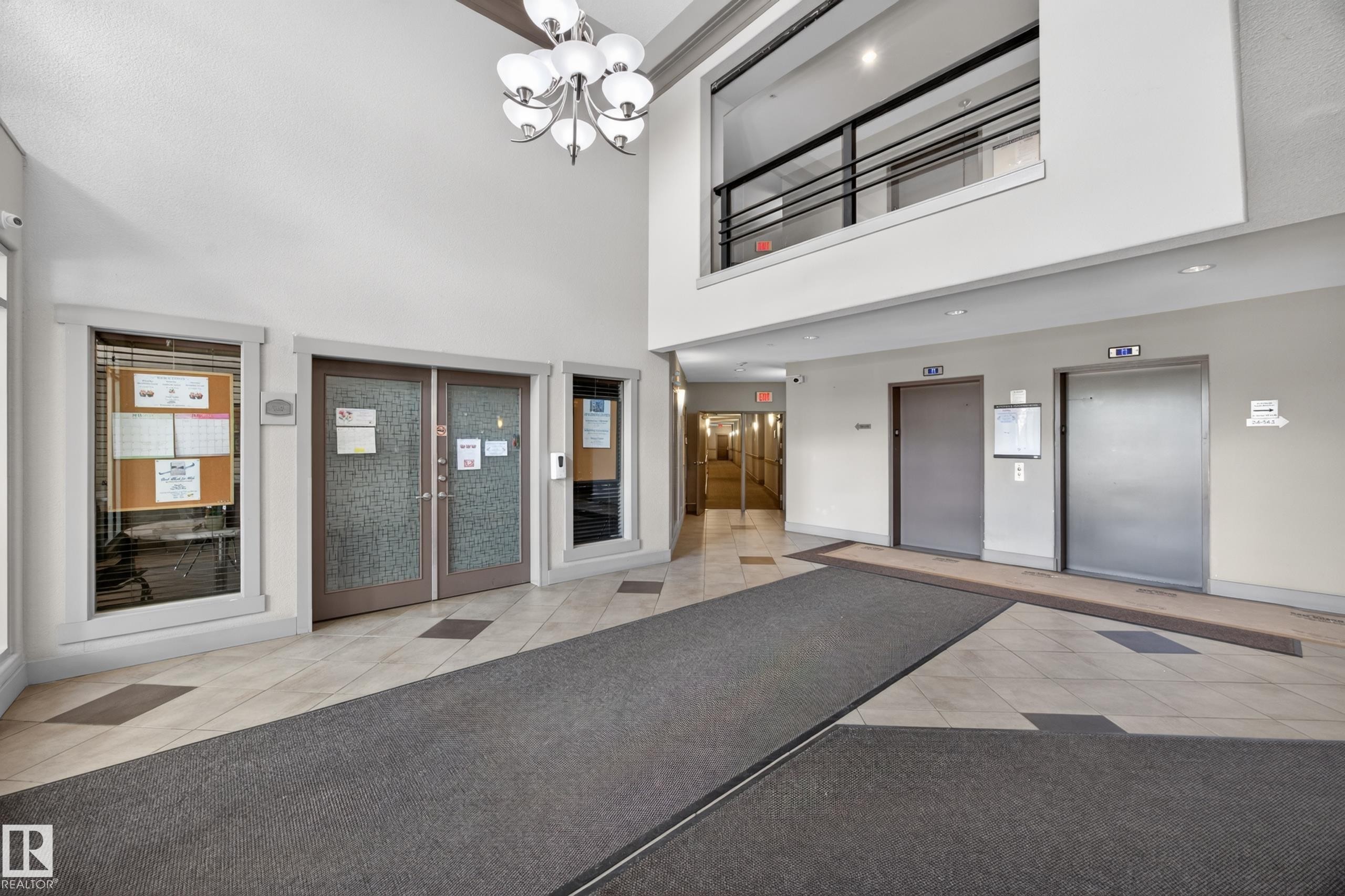 Spacious lobby featuring a high ceiling, two elevators, tile flooring, and a second-story interior balcony with metal railings - 138 16035 132 Street, Edmonton, AB