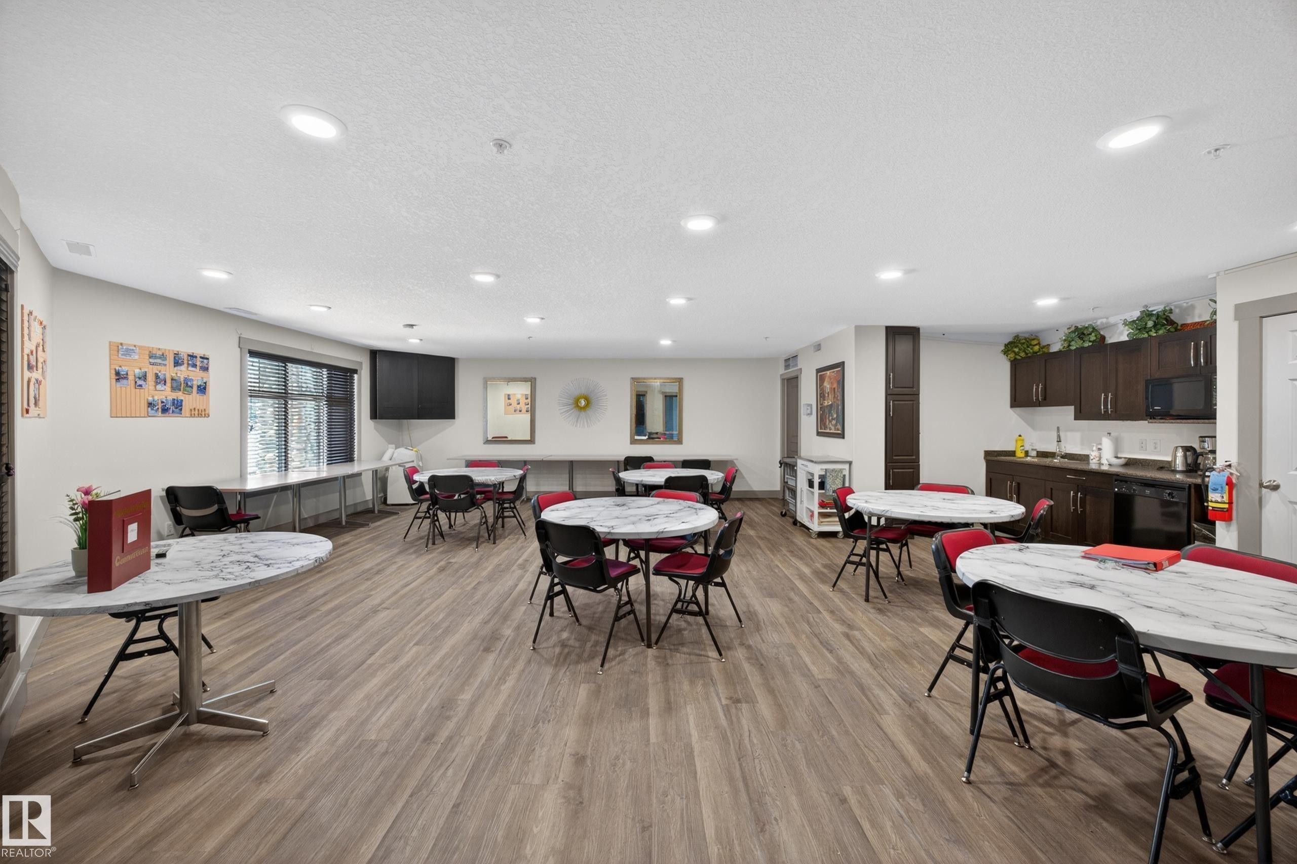 Spacious common area featuring wood-finish flooring, recessed lighting, and a full kitchen with dark cabinetry and black appliances - 138 16035 132 Street, Edmonton, AB