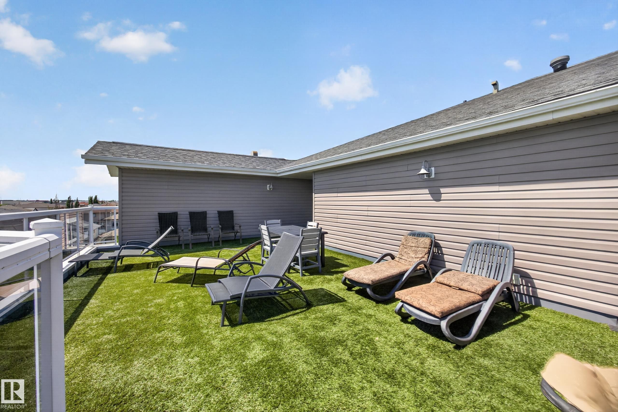Expansive rooftop deck featuring artificial turf, a white railing with glass panels, and exterior wall lighting - 138 16035 132 Street, Edmonton, AB