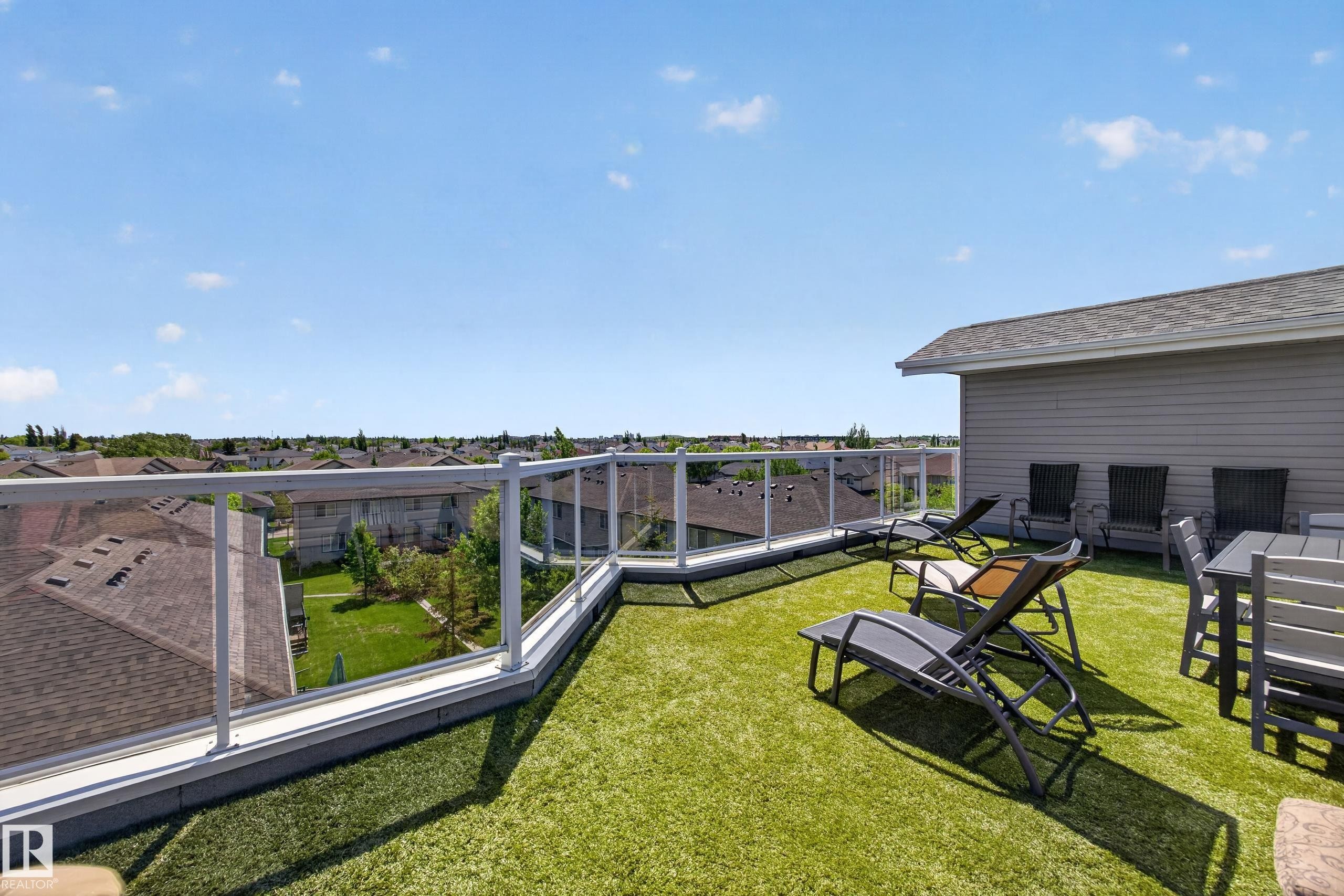 Expansive rooftop deck featuring artificial turf, clear glass railings, and a partial exterior wall with horizontal siding - 138 16035 132 Street, Edmonton, AB