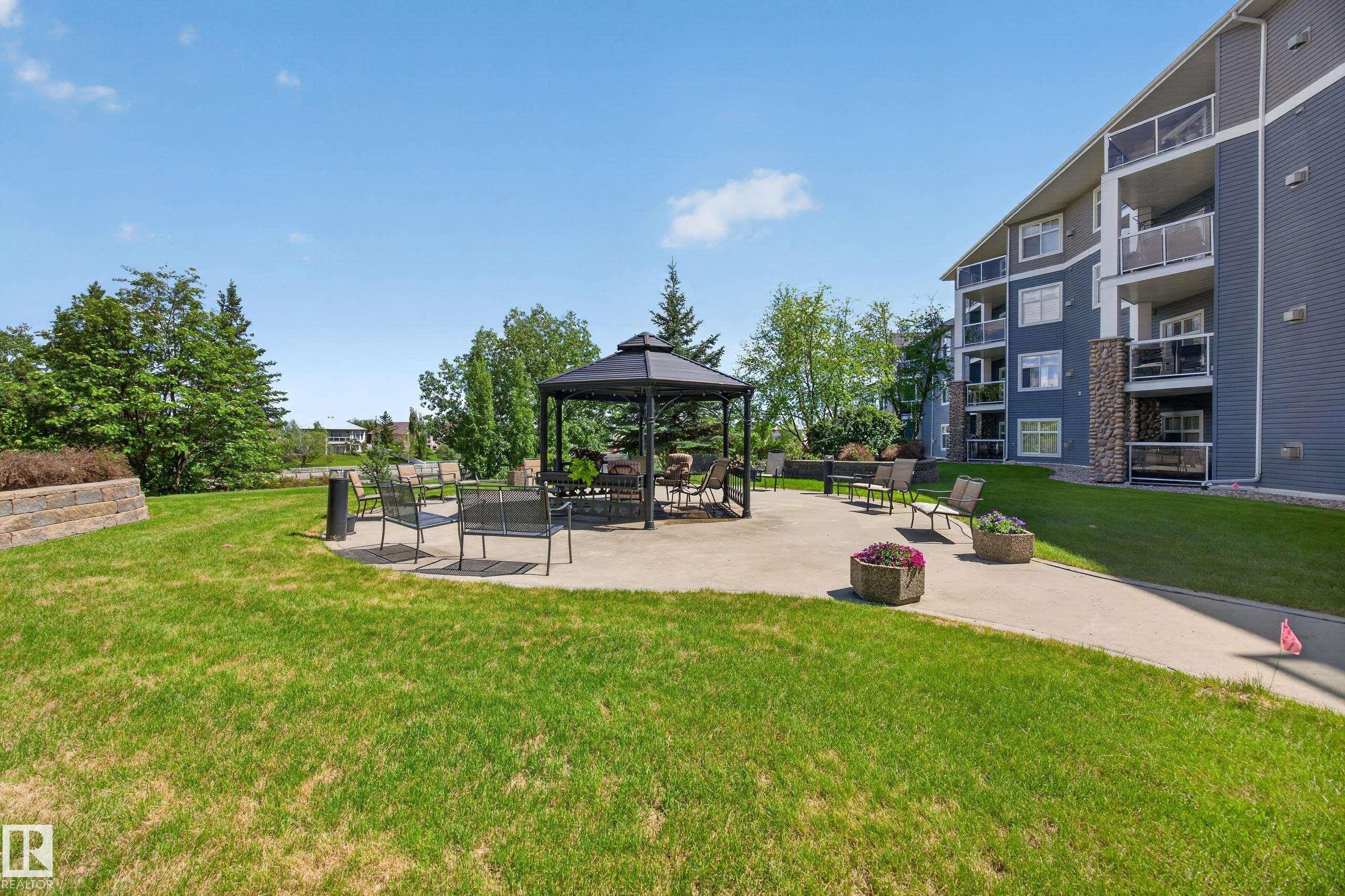 Outdoor common area featuring a central gazebo with seating, surrounded by a concrete patio and manicured lawn - 138 16035 132 Street, Edmonton, AB