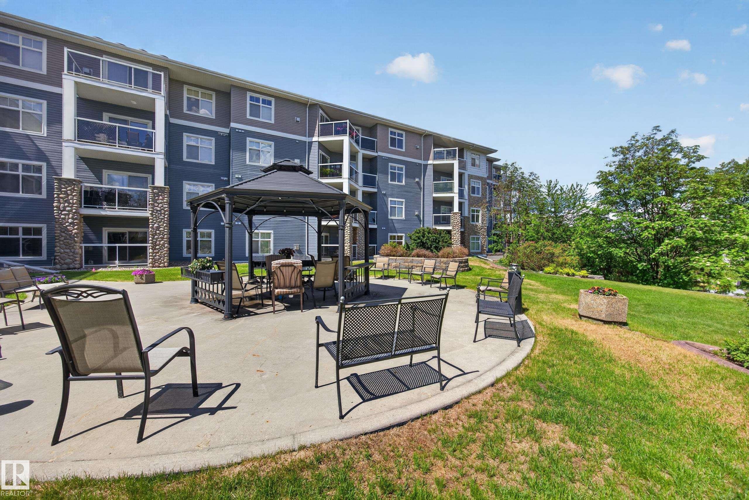 Outdoor patio area featuring a fixed gazebo, concrete hardscaping, and surrounding green space - 138 16035 132 Street, Edmonton, AB