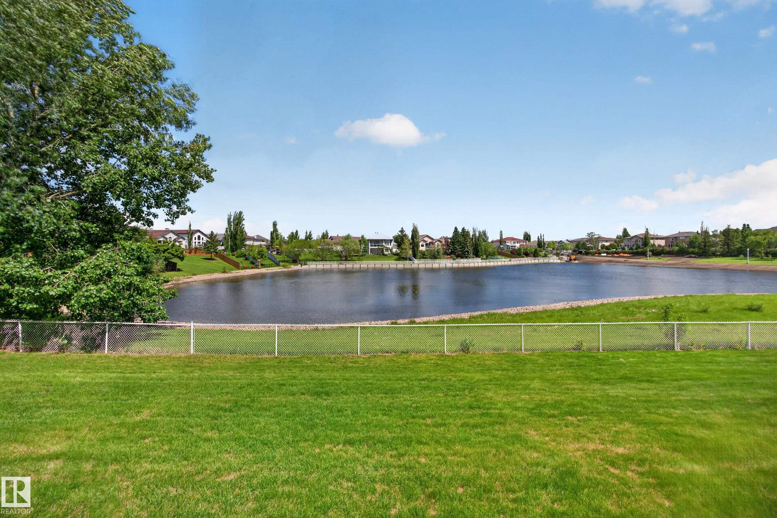 Expansive green lawn with a chain-link fence bordering a large body of water - 138 16035 132 Street, Edmonton, AB