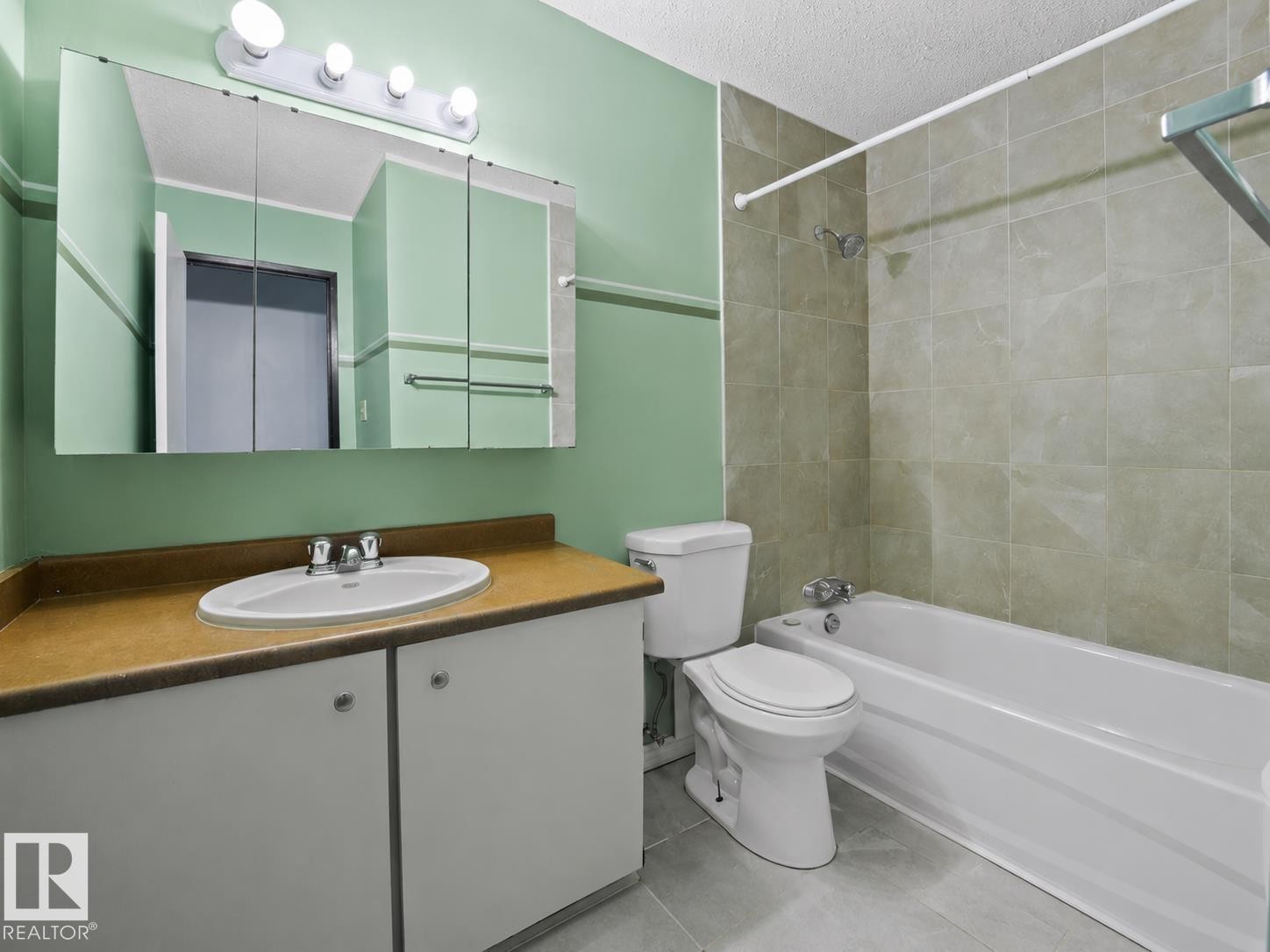 Vanity with an integrated sink, medicine cabinet with overhead lighting, tiled tub surround, and tile flooring - #1 13450 Fort Rd Nw, Edmonton, AB - Indoor Photo Showing Bathroom