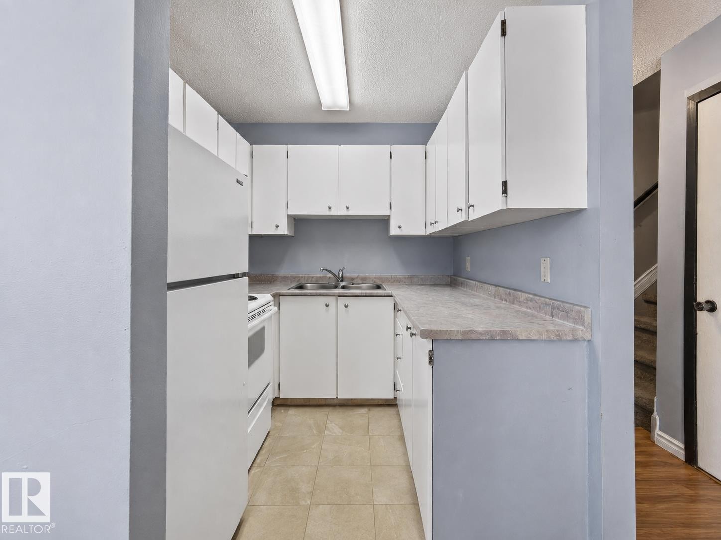 Compact kitchen with white cabinetry, light-toned countertops, and a double basin sink - #1 13450 Fort Rd Nw, Edmonton, AB - Indoor Photo Showing Kitchen With Double Sink