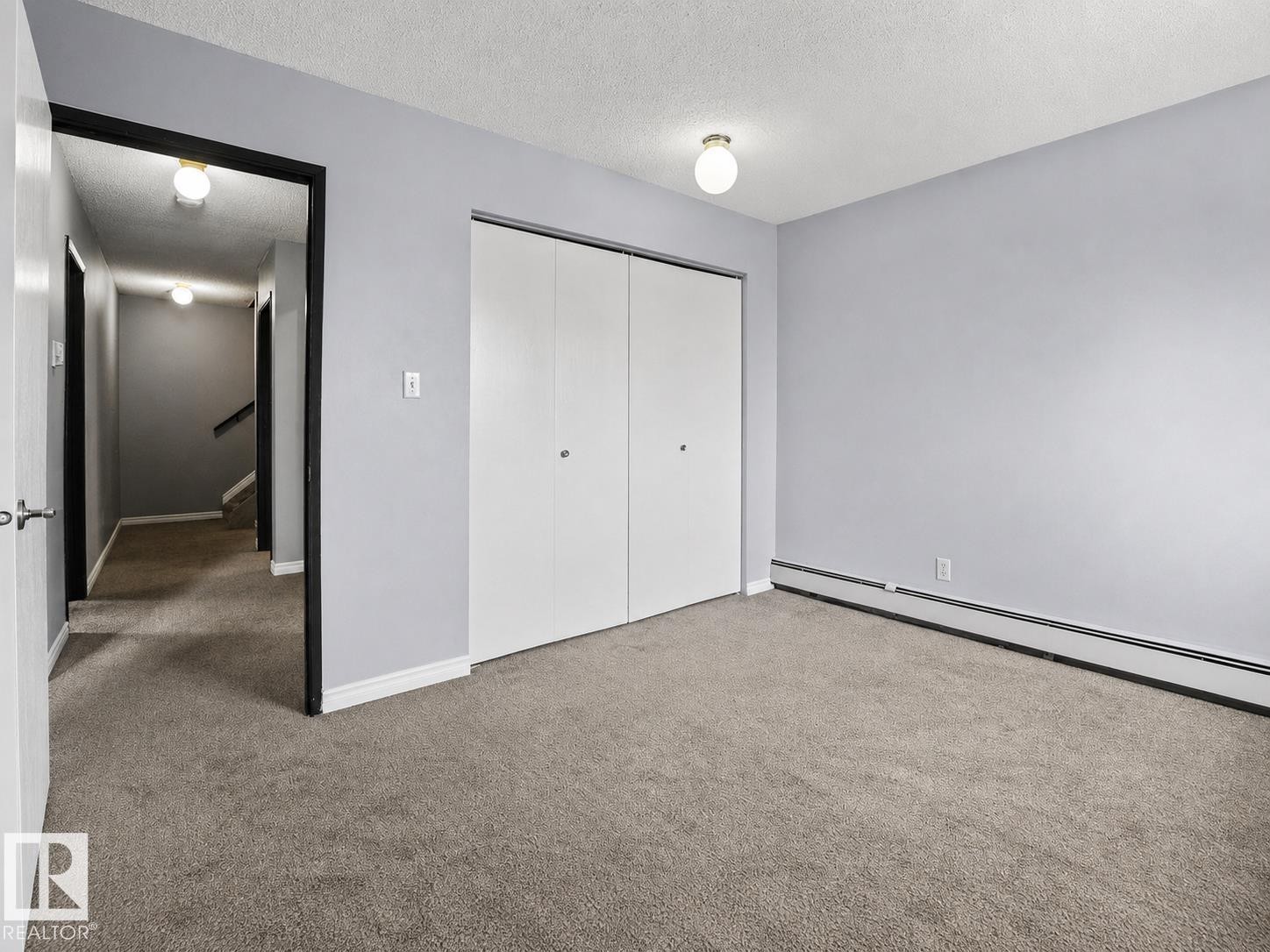 Carpeted flooring, bi-fold closet doors, wall-mounted baseboard heating, ceiling-mounted light fixture - #1 13450 Fort Rd Nw, Edmonton, AB - Indoor Photo Showing Other Room