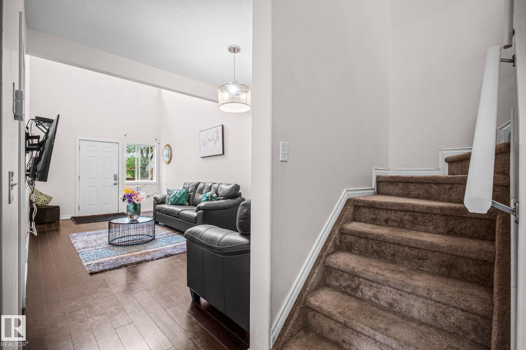 Living area with wood-finish flooring, vaulted ceiling, and a white paneled entry door - 4806 117 Ave, Edmonton, AB