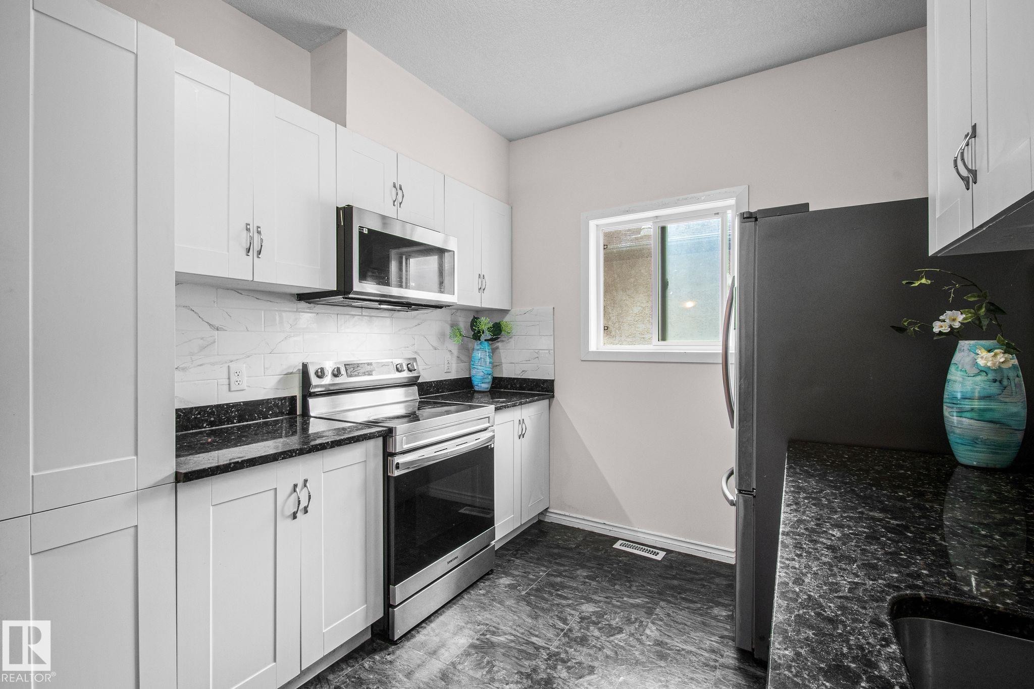 Kitchen featuring white shaker-style cabinetry, dark granite-look countertops, and a white tile backsplash - 4806 117 Ave, Edmonton, AB