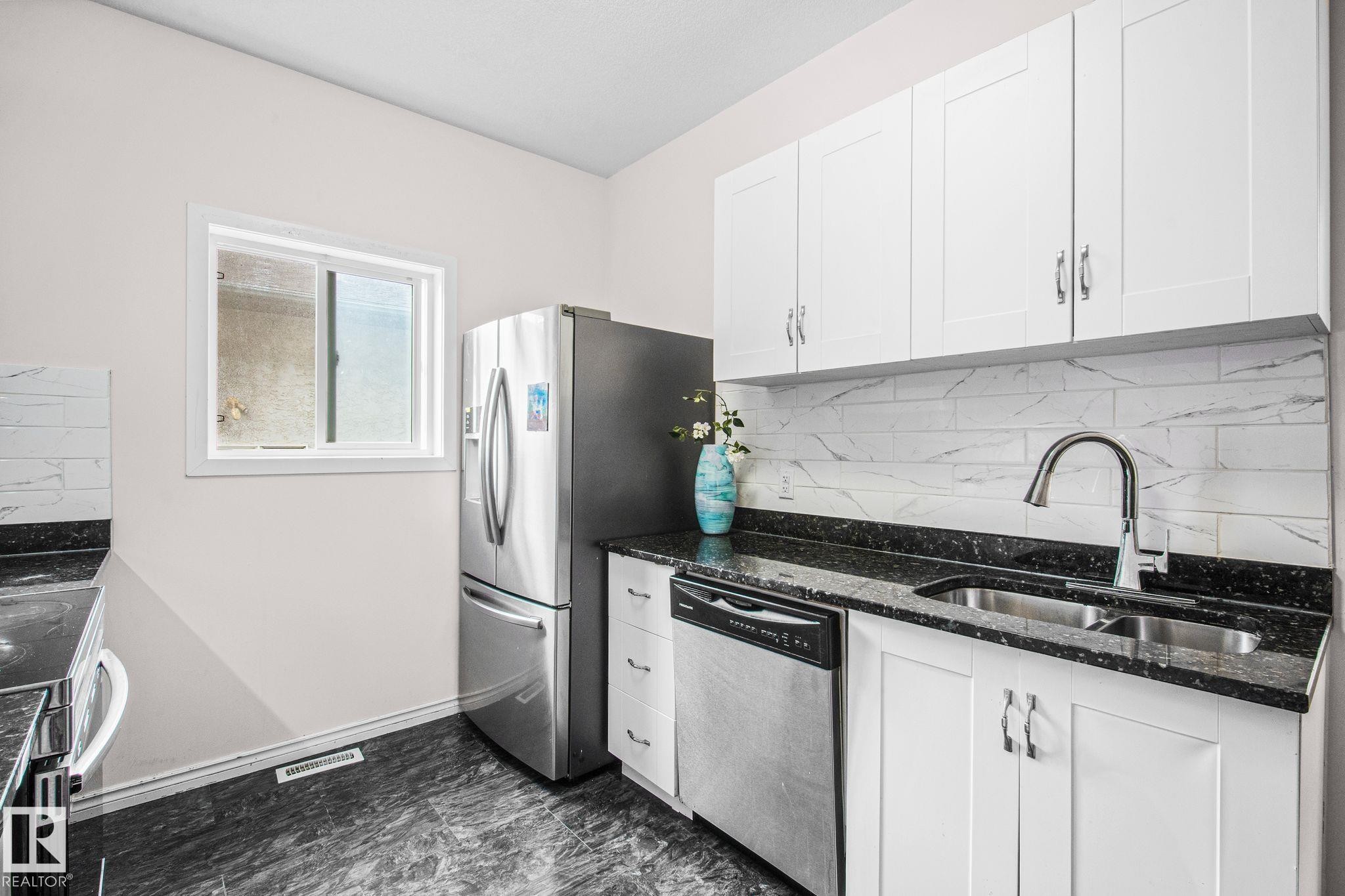 Kitchen featuring white upper cabinetry, stainless steel appliances, dark speckled countertops, and a white subway tile backsplash - 4806 117 Ave, Edmonton, AB