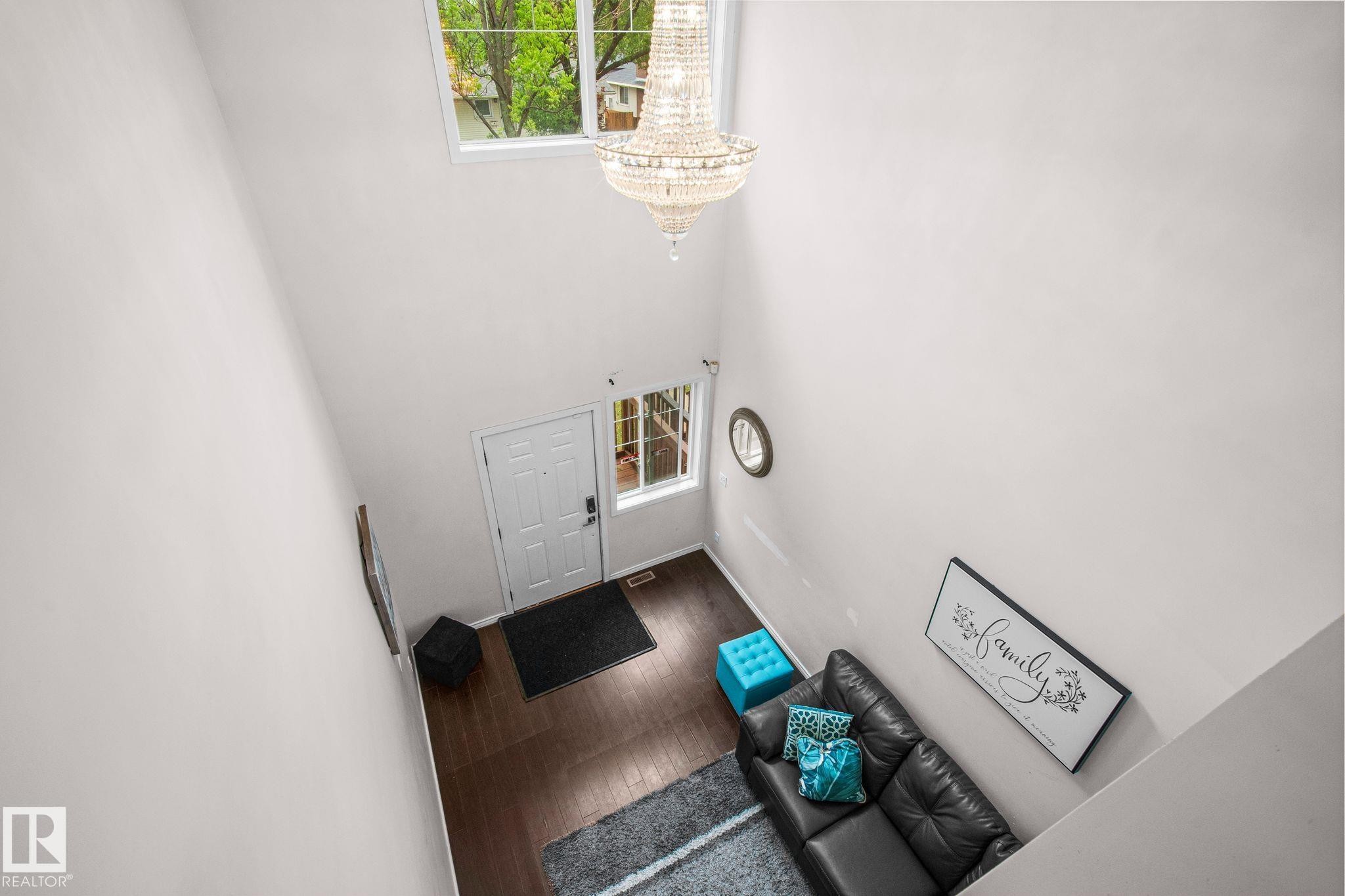 Two-story entryway featuring a crystal chandelier, upper-level window, white entry door with sidelights, and dark wood-finish flooring - 4806 117 Ave, Edmonton, AB