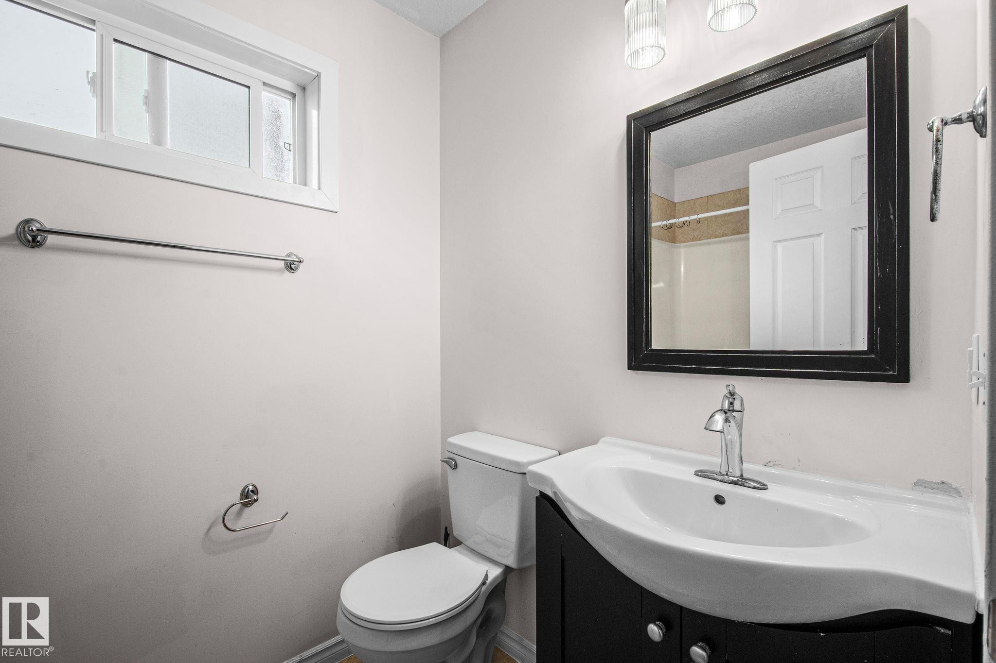 Bathroom featuring a dark wood-finish vanity with an integrated white sink, a framed mirror, and chrome fixtures - 4806 117 Ave, Edmonton, AB
