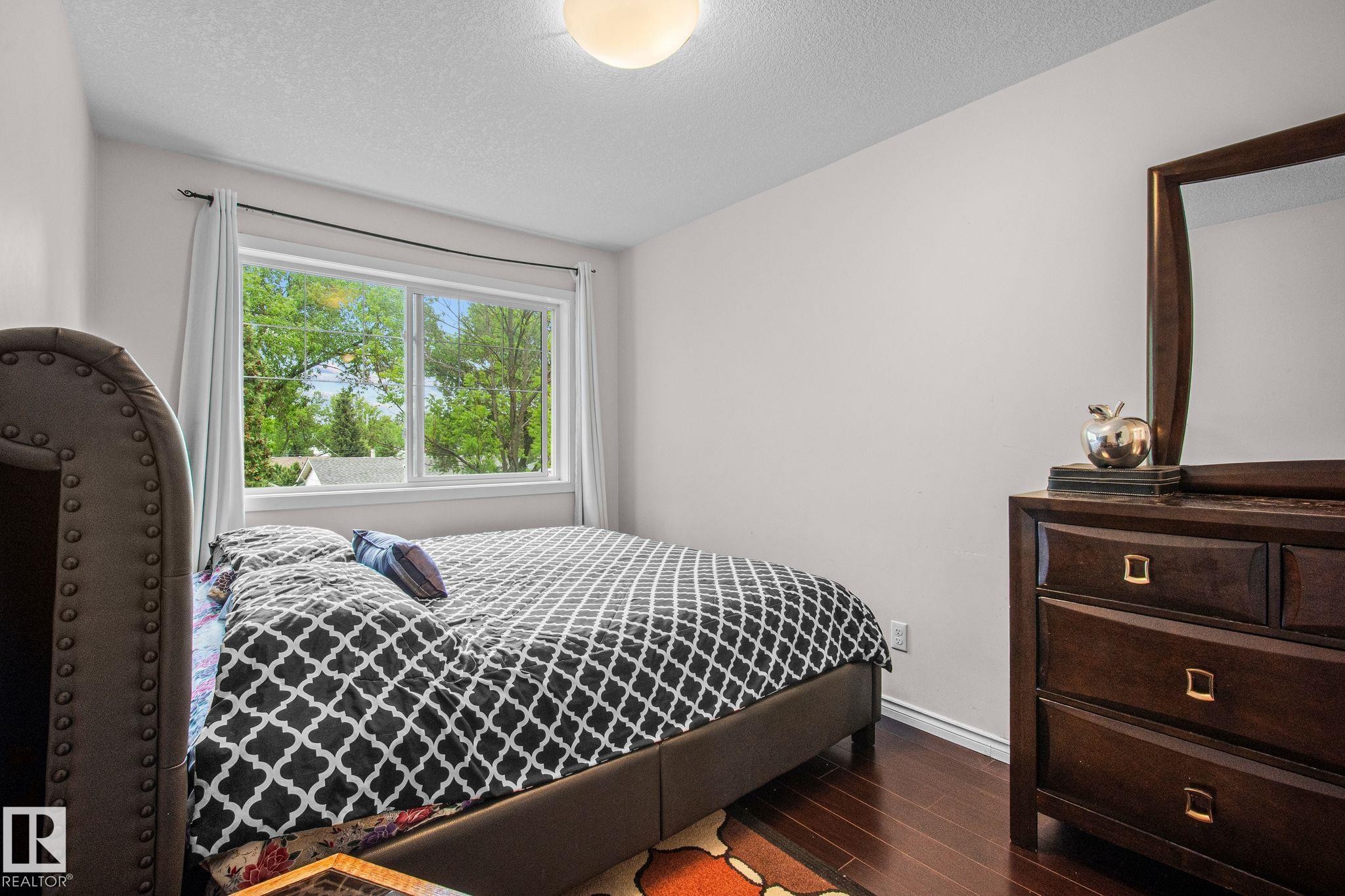 Bedroom featuring a large window with white trim, dark wood-finish flooring, and a flush mount ceiling light - 4806 117 Ave, Edmonton, AB