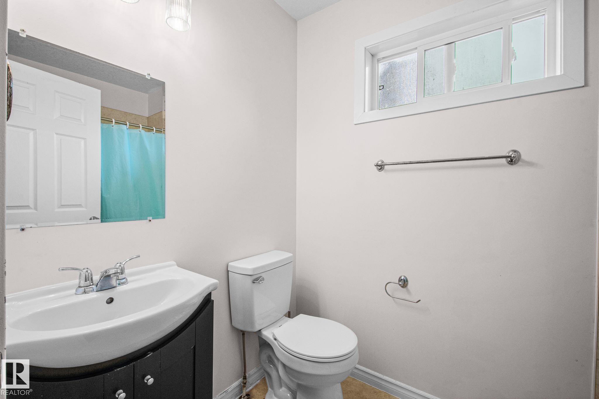 Bathroom featuring a dark wood-finish vanity with a white basin sink, chrome faucet, and mirrored wall - 4806 117 Ave, Edmonton, AB