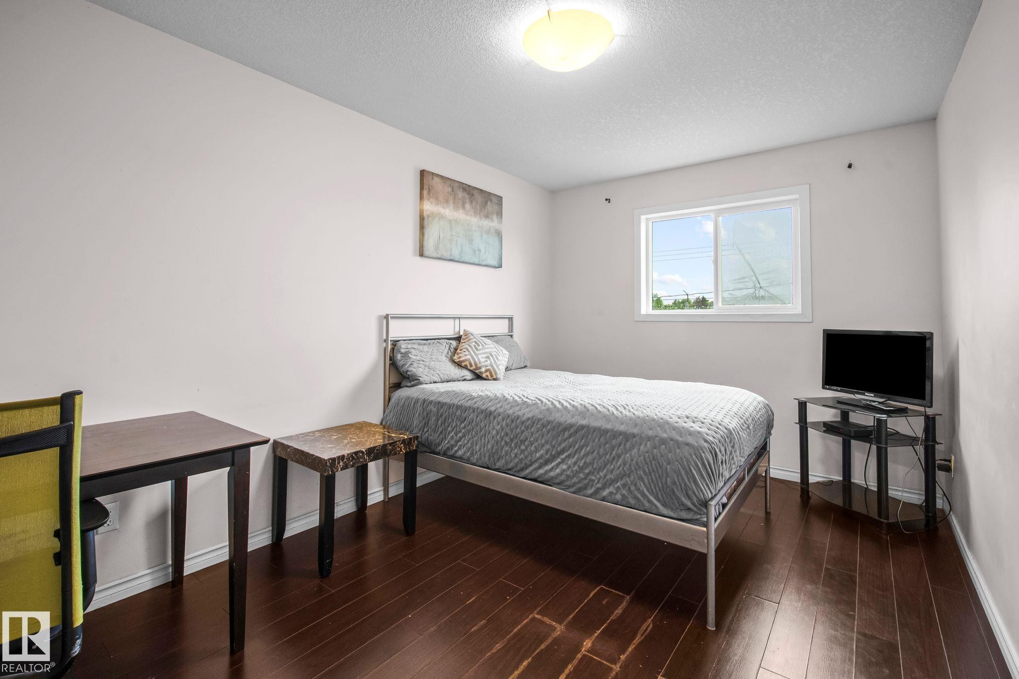 Bedroom featuring dark wood-finish flooring, a white-framed window, and a flush-mount ceiling light - 4806 117 Ave, Edmonton, AB
