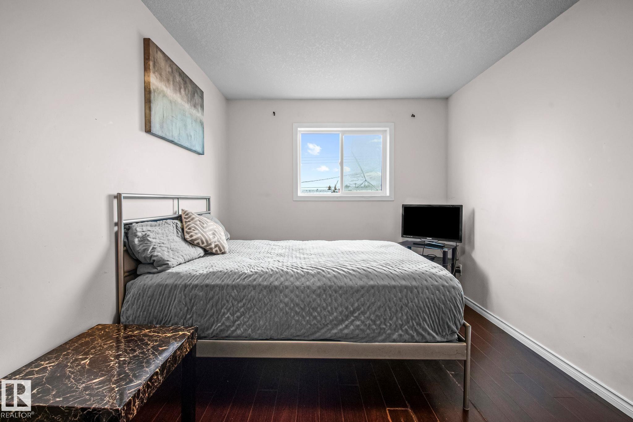 Bedroom featuring a window with natural light, dark wood-finish flooring, and white baseboards - 4806 117 Ave, Edmonton, AB