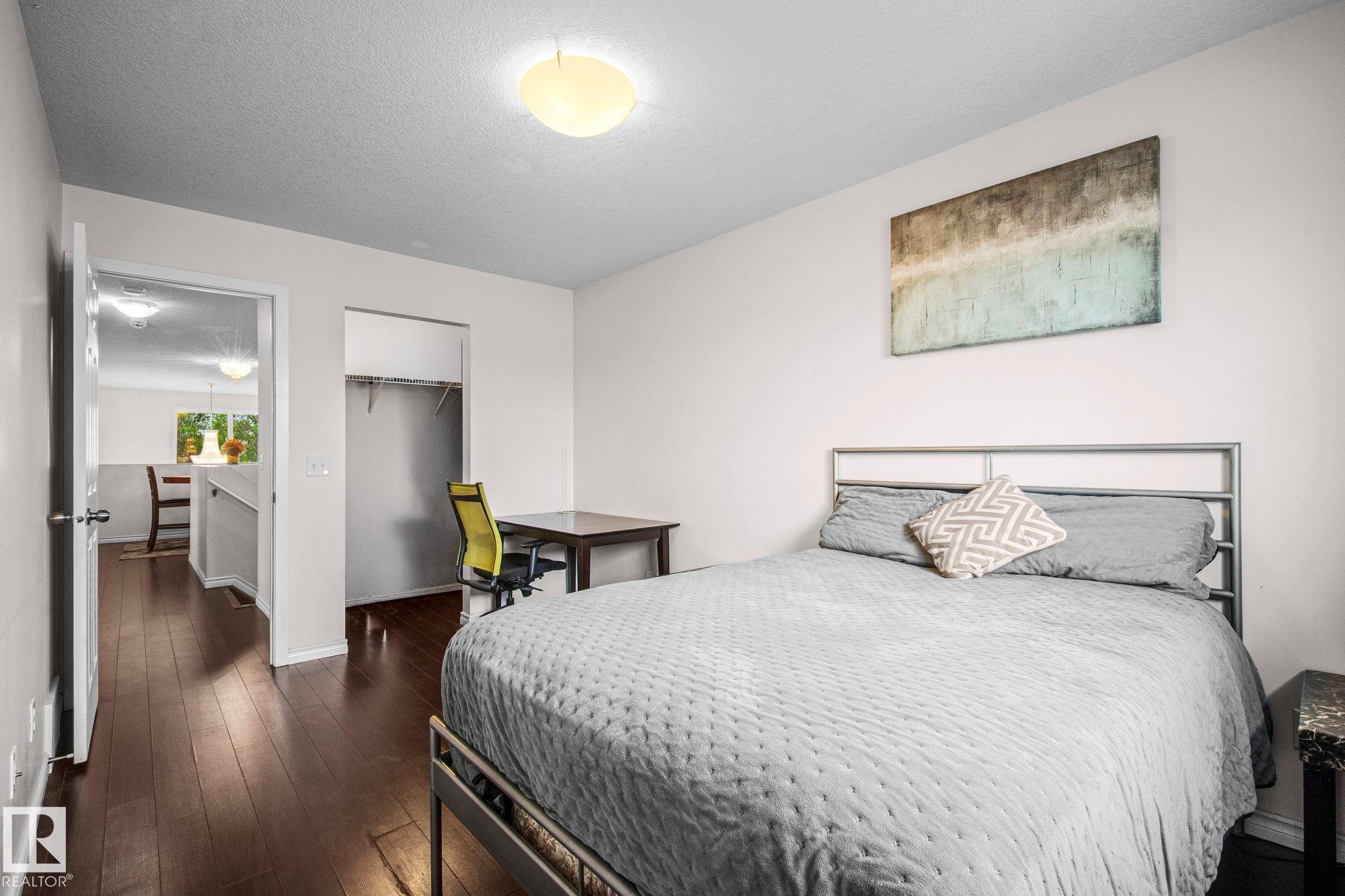Spacious room featuring dark wood-finish flooring, a ceiling-mounted light fixture, an open doorway, and an open closet with built-in shelving - 4806 117 Ave, Edmonton, AB