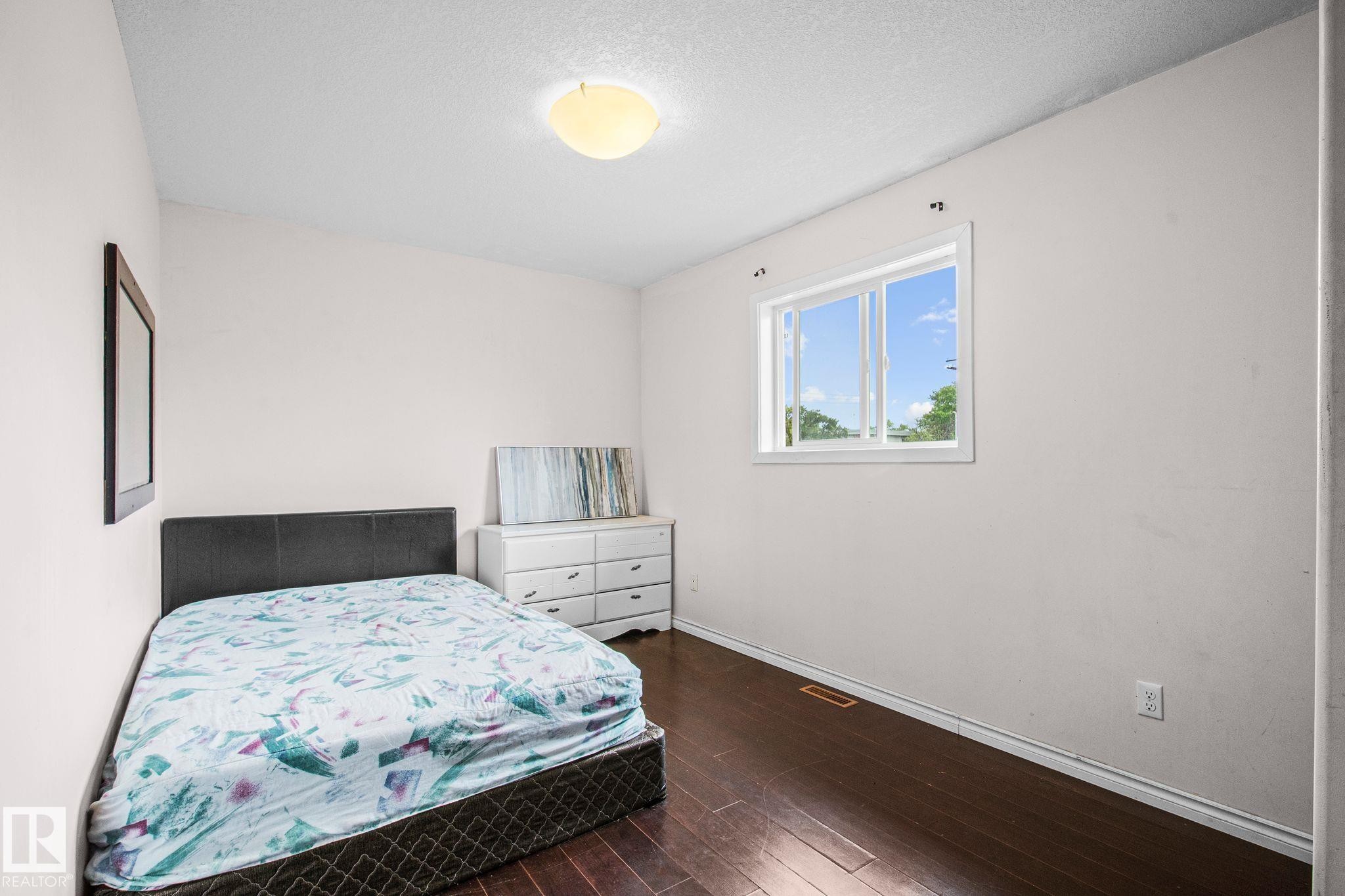 Bedroom featuring dark wood-finish flooring, white baseboards, and a white ceiling with a flush-mount light fixture - 4806 117 Ave, Edmonton, AB