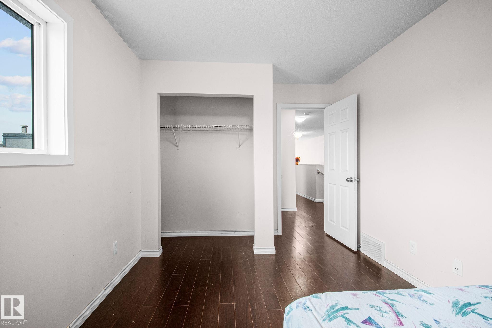 Interior room featuring wood-finish flooring, a white trim window, a full closet with shelving, a white paneled door, and neutral wall tones - 4806 117 Ave, Edmonton, AB