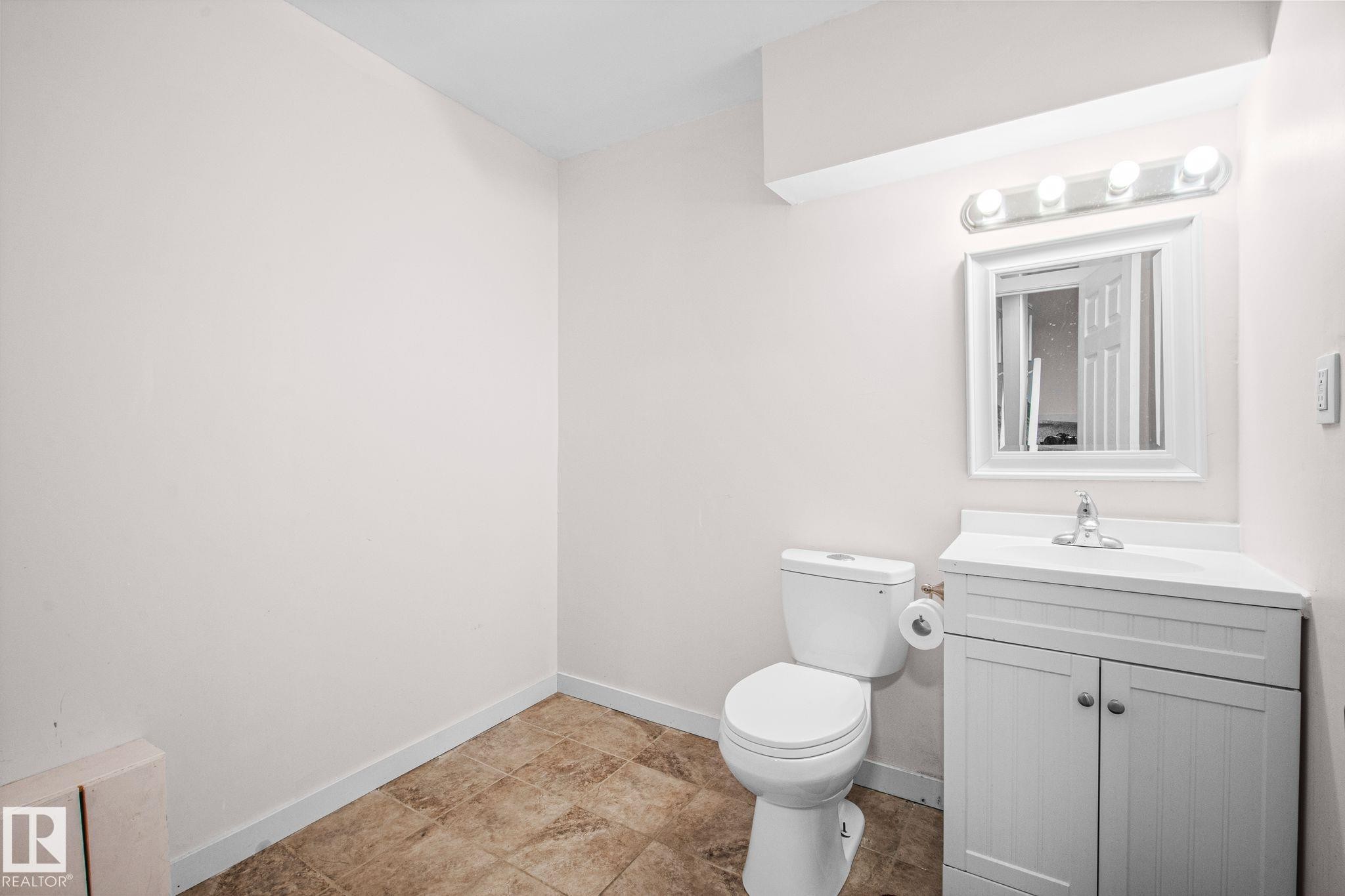 Bathroom featuring a white vanity with cabinet storage, a white countertop, and a framed mirror - 4806 117 Ave, Edmonton, AB