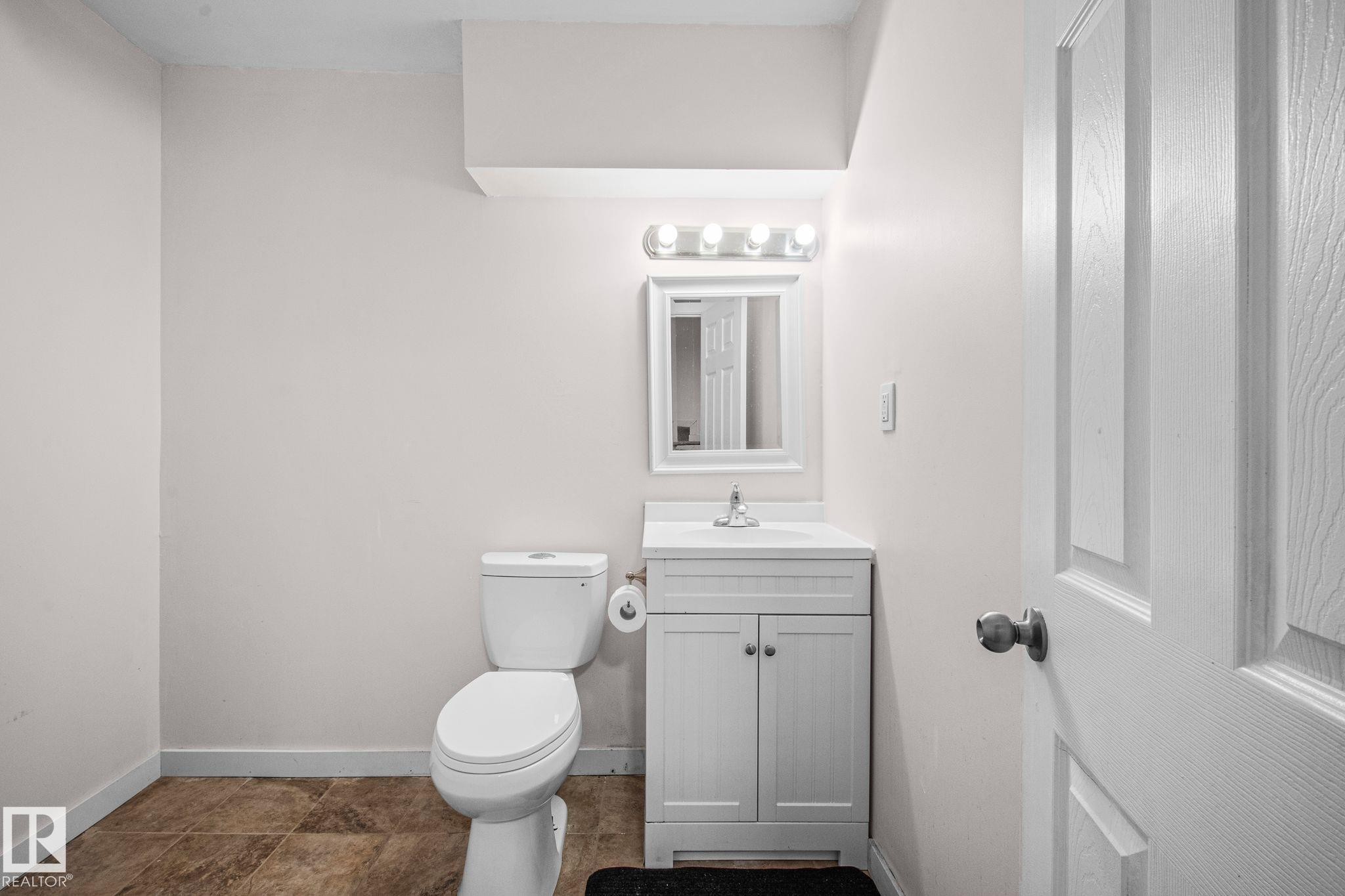 Powder room featuring a white single-sink vanity with a chrome faucet, wall-mounted mirror, and overhead vanity lighting - 4806 117 Ave, Edmonton, AB