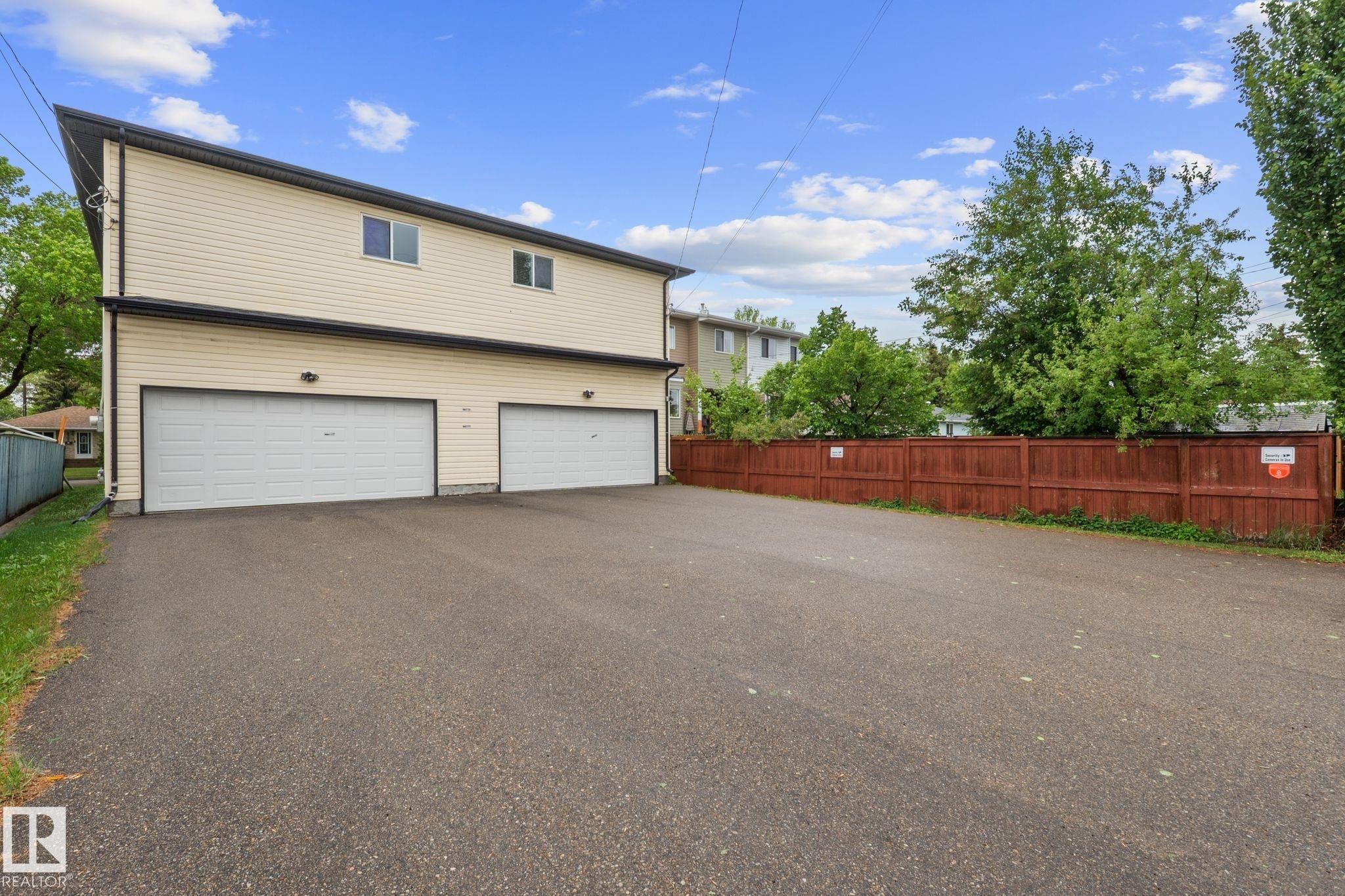 Cream-colored siding building featuring two ground-level garage doors, upper-level windows, and a dark trim - 4806 117 Ave, Edmonton, AB