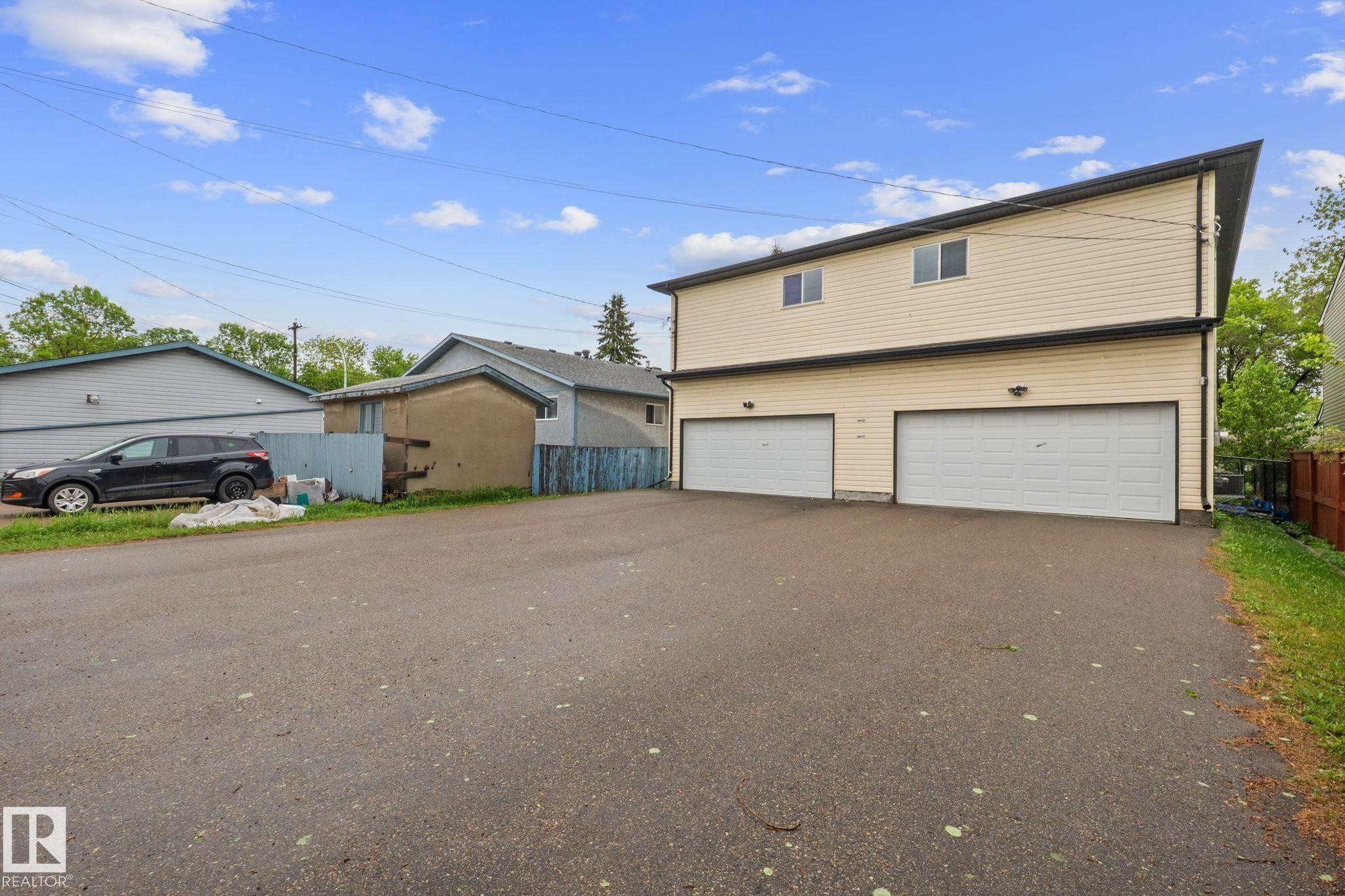 Two-story structure featuring light-colored siding, a dark roofline, and two garage doors - 4806 117 Ave, Edmonton, AB