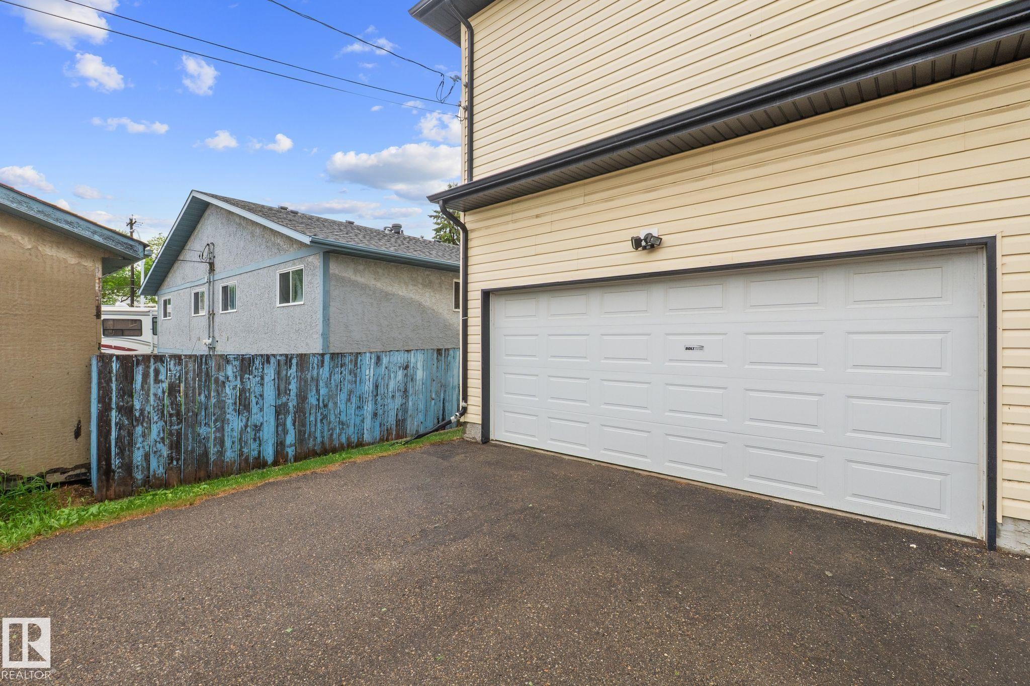 Attached garage featuring a white panel door, light-colored horizontal siding, dark gutters, and exterior lighting - 4806 117 Ave, Edmonton, AB