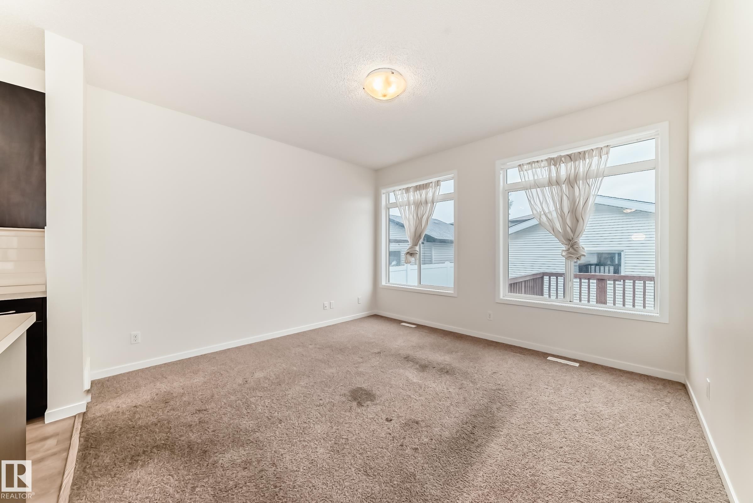 Open-concept room featuring two large windows, white trim, and a semi-flush mount ceiling light - 18103 77 Street, Edmonton, AB