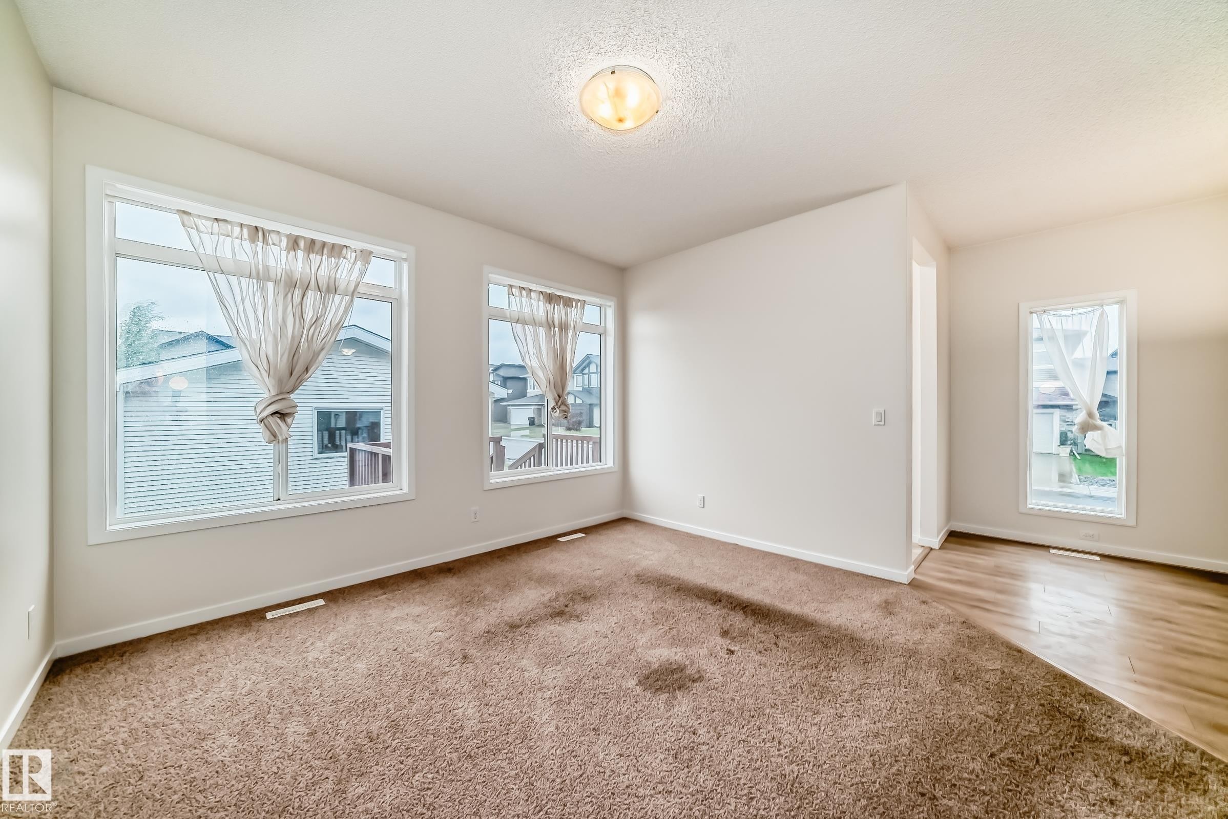 Spacious interior featuring large windows, neutral paint, a combination of carpet and wood-finish flooring, and a ceiling-mounted light fixture - 18103 77 Street, Edmonton, AB