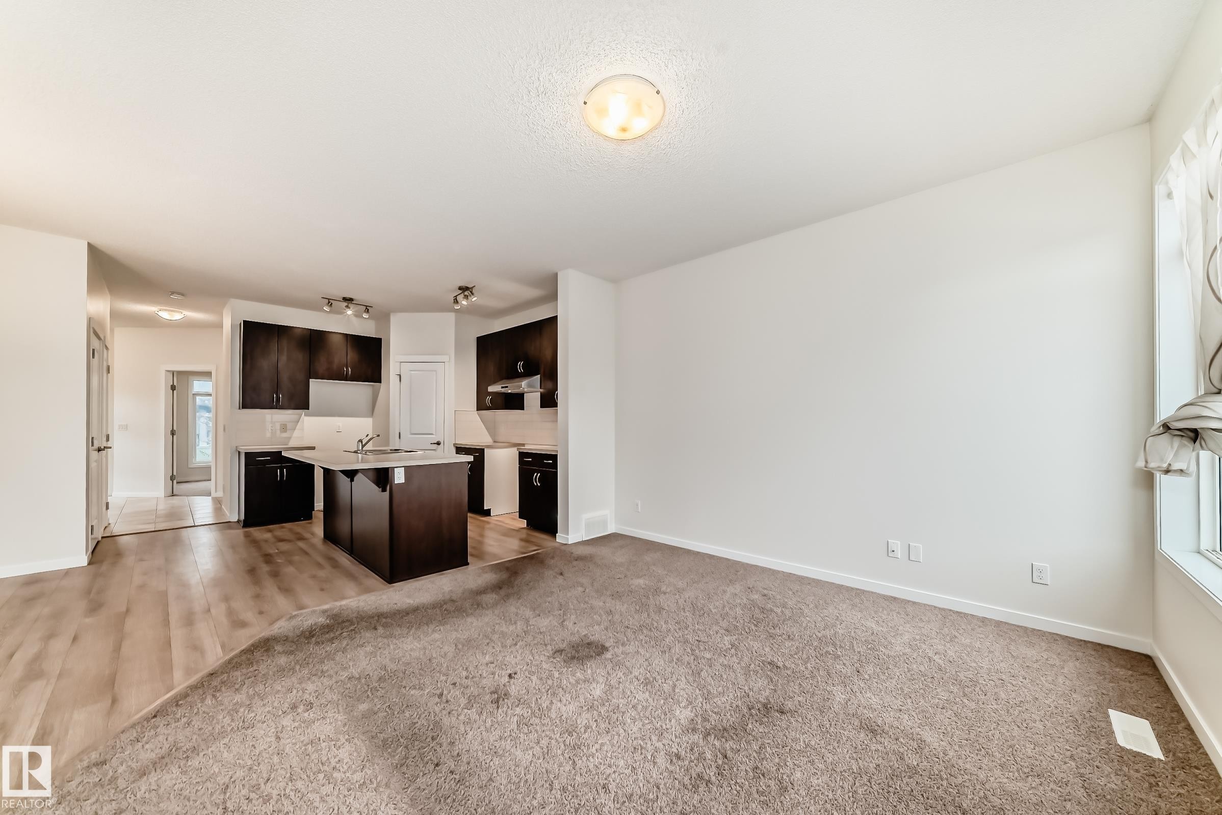 Open-concept living space featuring a kitchen with dark wood-finish cabinetry, a central island with an undermount sink, and track lighting - 18103 77 Street, Edmonton, AB