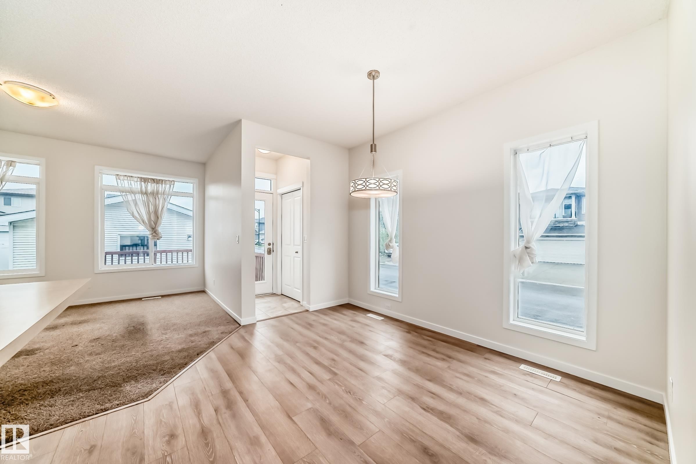Interior space featuring wood-finish flooring, a contemporary pendant light fixture, and multiple windows with white trim - 18103 77 Street, Edmonton, AB
