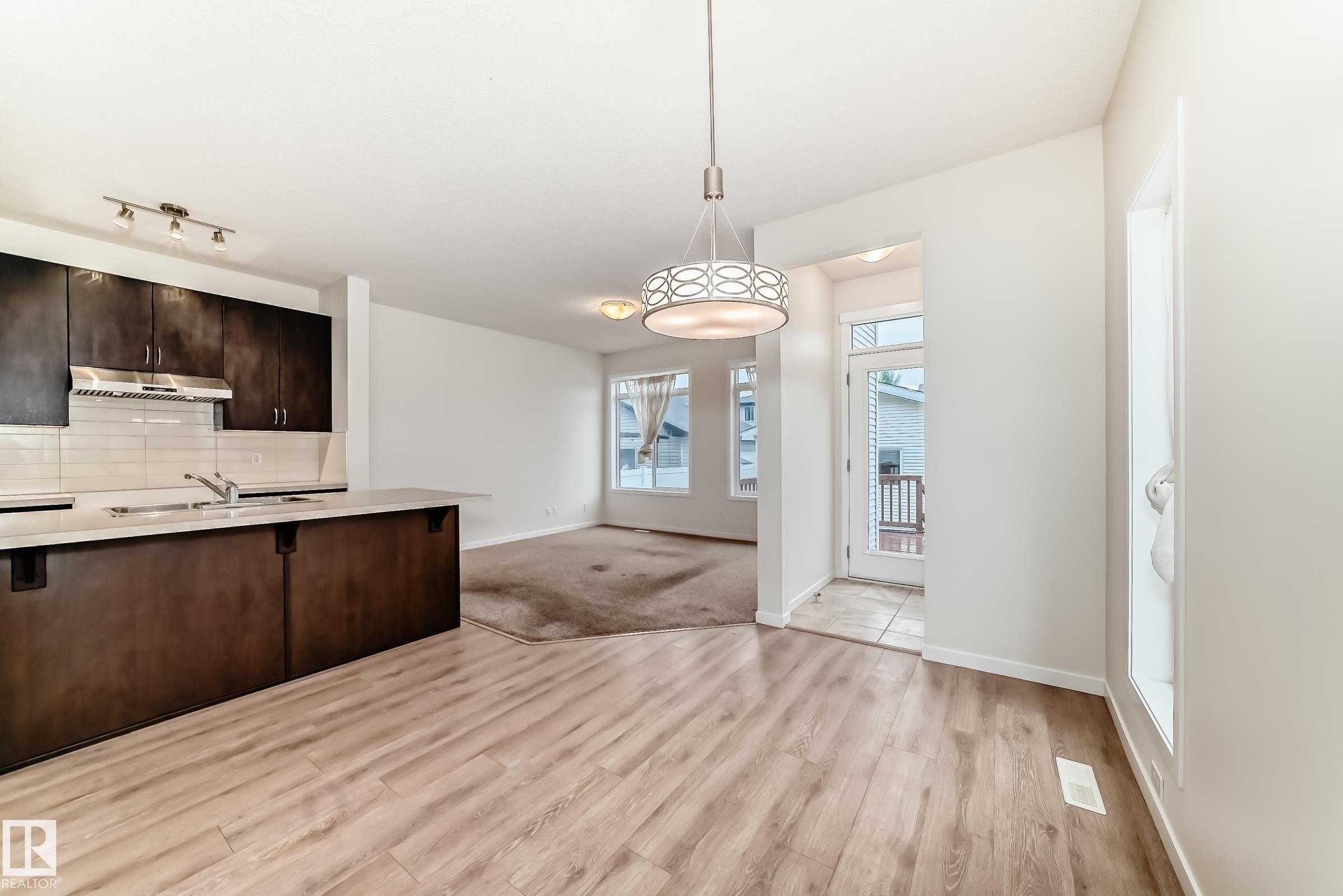 Open-concept interior featuring wood-finish flooring, a kitchen island with sink and light countertop, dark wood cabinetry, and a subway tile backsplash - 18103 77 Street, Edmonton, AB