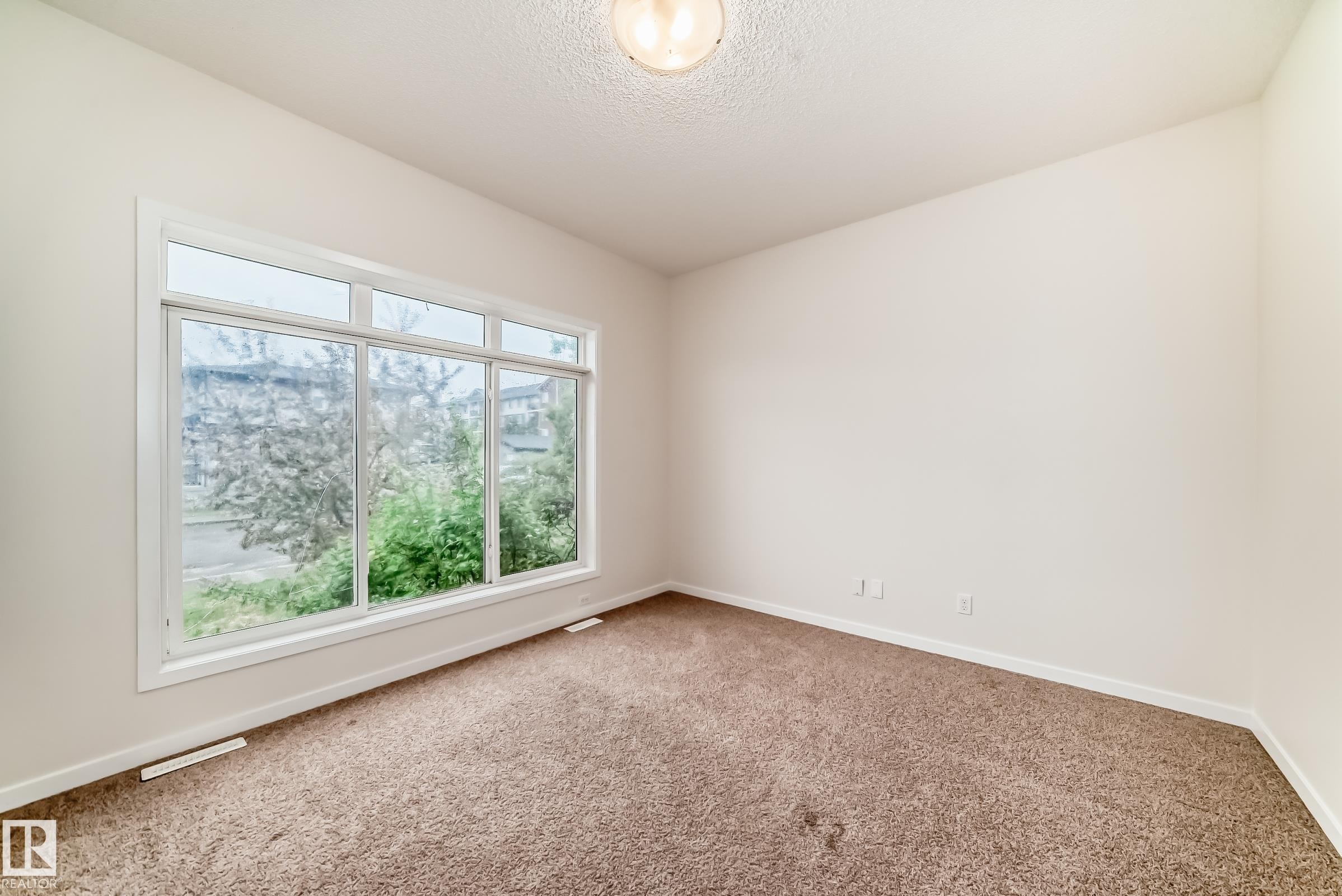 Bright interior space featuring a multi-pane window, neutral wall paint, textured ceiling, and brown carpeting - 18103 77 Street, Edmonton, AB