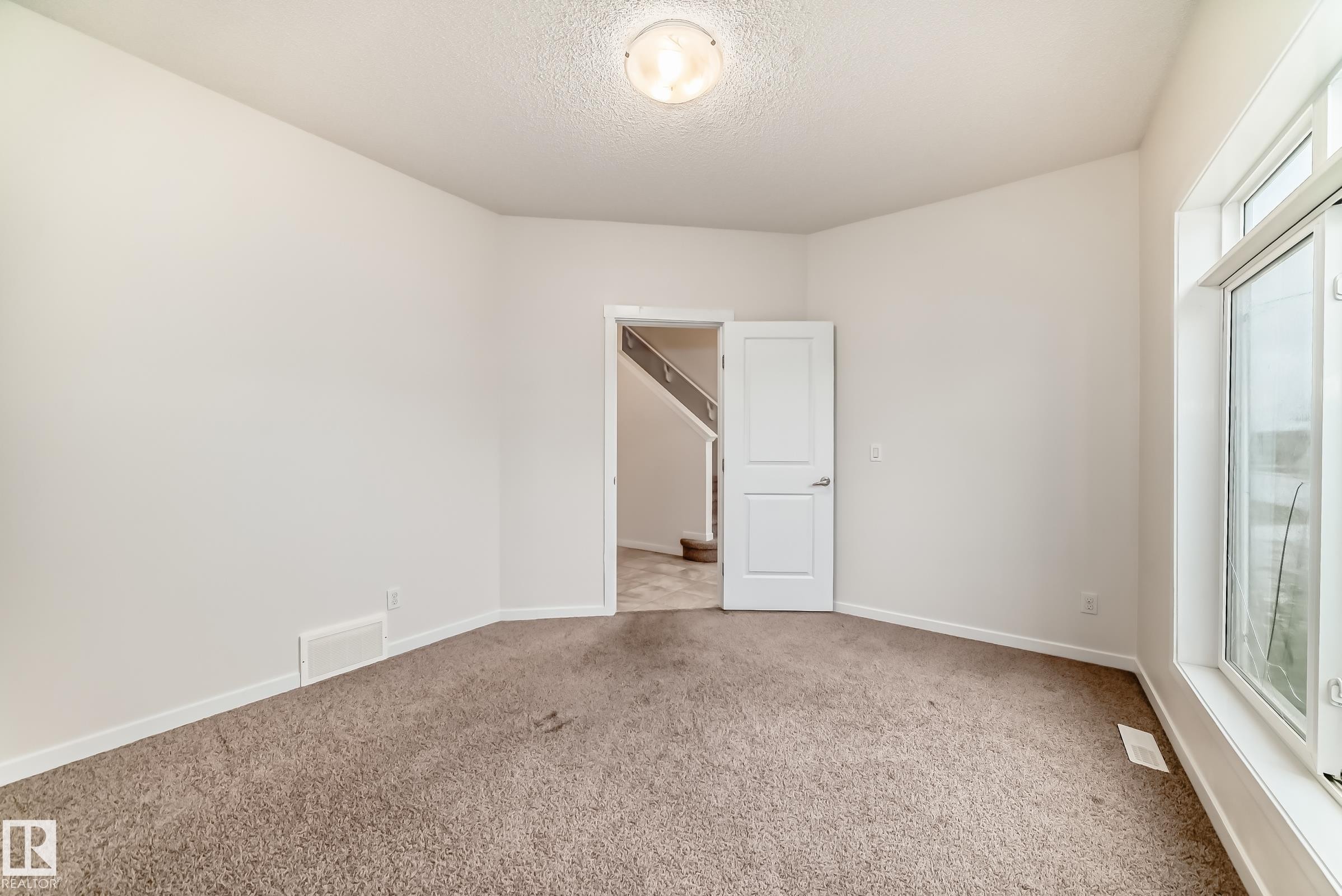 Carpeted room with white walls, a large window, a white interior door, and a flush-mount ceiling light fixture - 18103 77 Street, Edmonton, AB