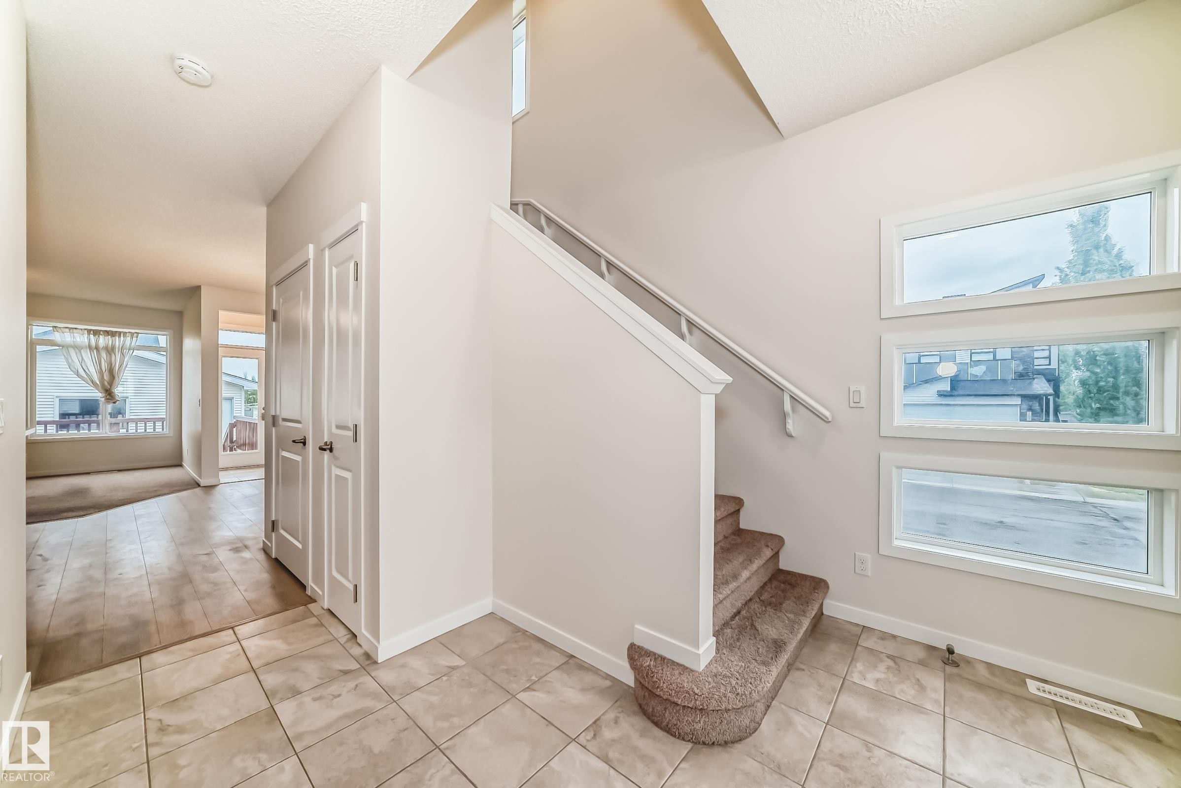 Entryway featuring tile flooring, a carpeted staircase with white railings, and three horizontal windows providing natural light - 18103 77 Street, Edmonton, AB