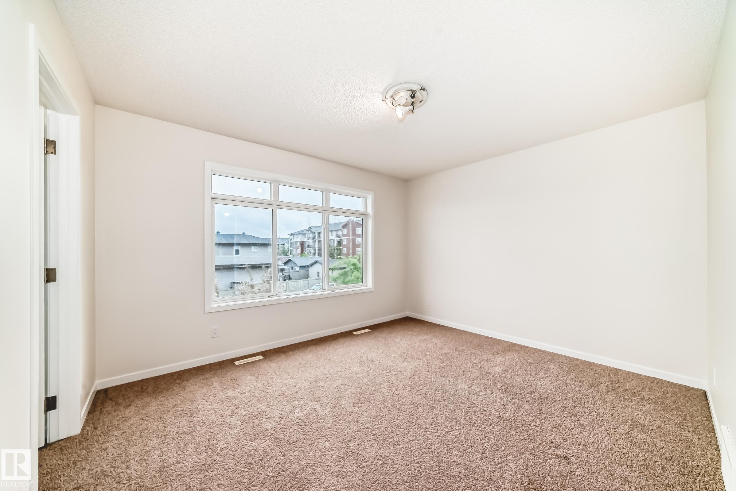Bright interior space featuring a large window, neutral wall tones, and plush carpet flooring - 18103 77 Street, Edmonton, AB