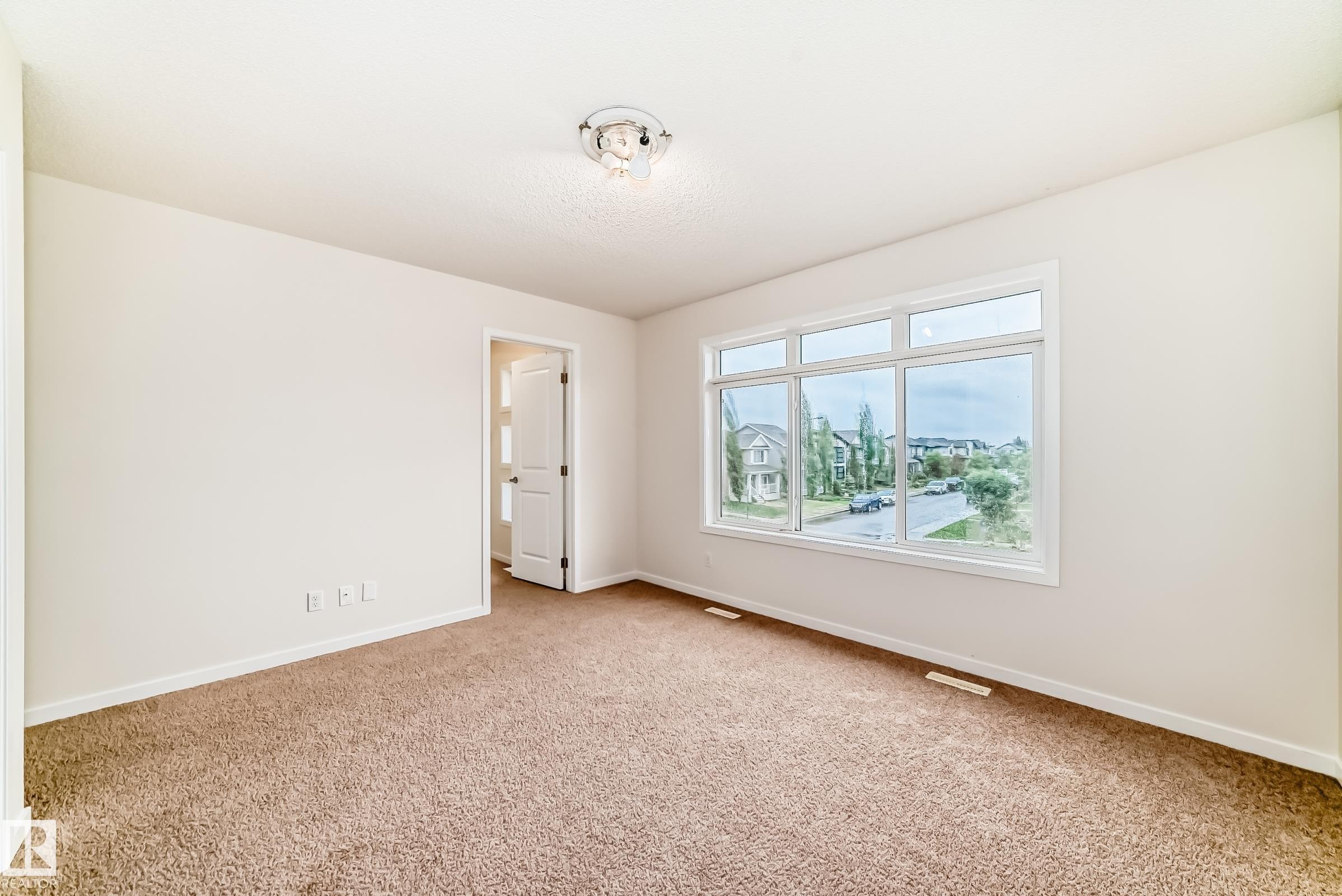 Bright room featuring a large multi-pane window, neutral-toned carpet, and a white interior door - 18103 77 Street, Edmonton, AB