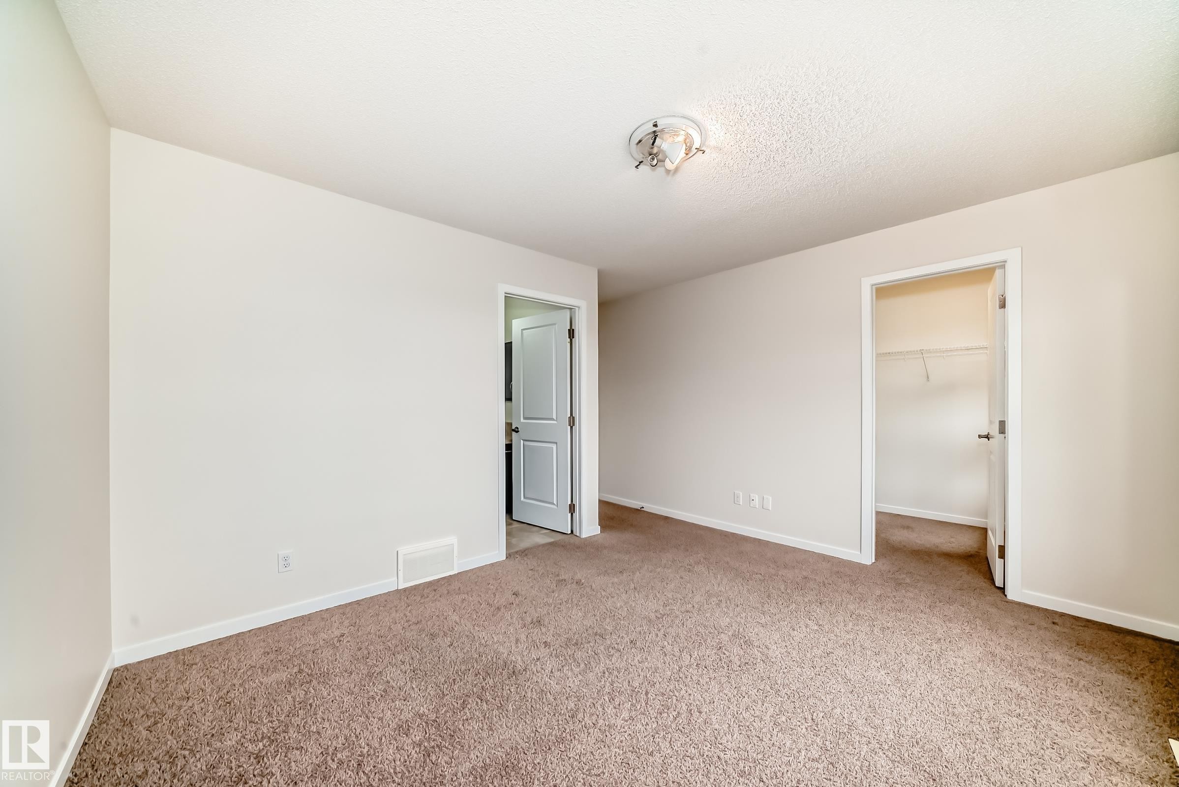 Carpeted room featuring neutral wall tones, white trim, a ceiling-mounted light fixture, and two interior doors - 18103 77 Street, Edmonton, AB