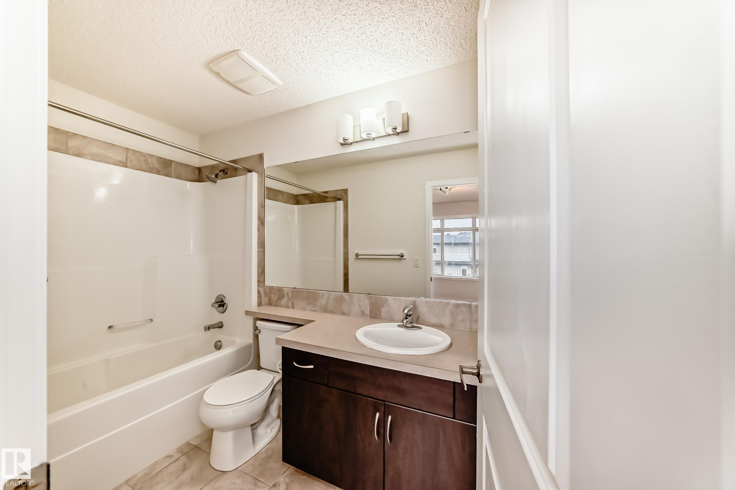 Full bathroom featuring a white tub and shower combination with tiled surround, a vanity with a white basin and light-toned countertop, and a large mirror with overhead lighting - 18103 77 Street, Edmonton, AB
