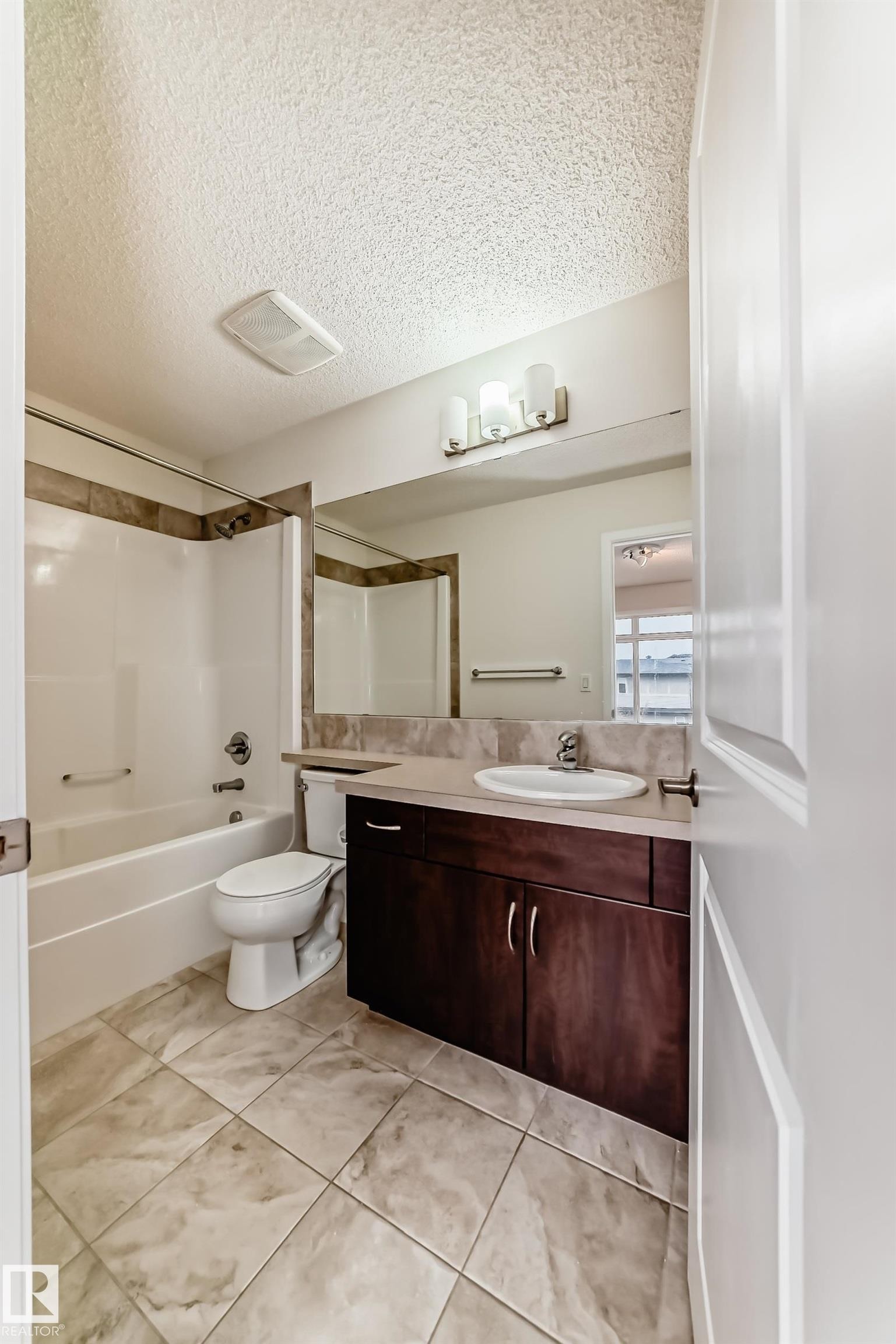 Bathroom featuring a wood-finish vanity with an integrated sink, a large wall mirror, and a three-light fixture - 18103 77 Street, Edmonton, AB