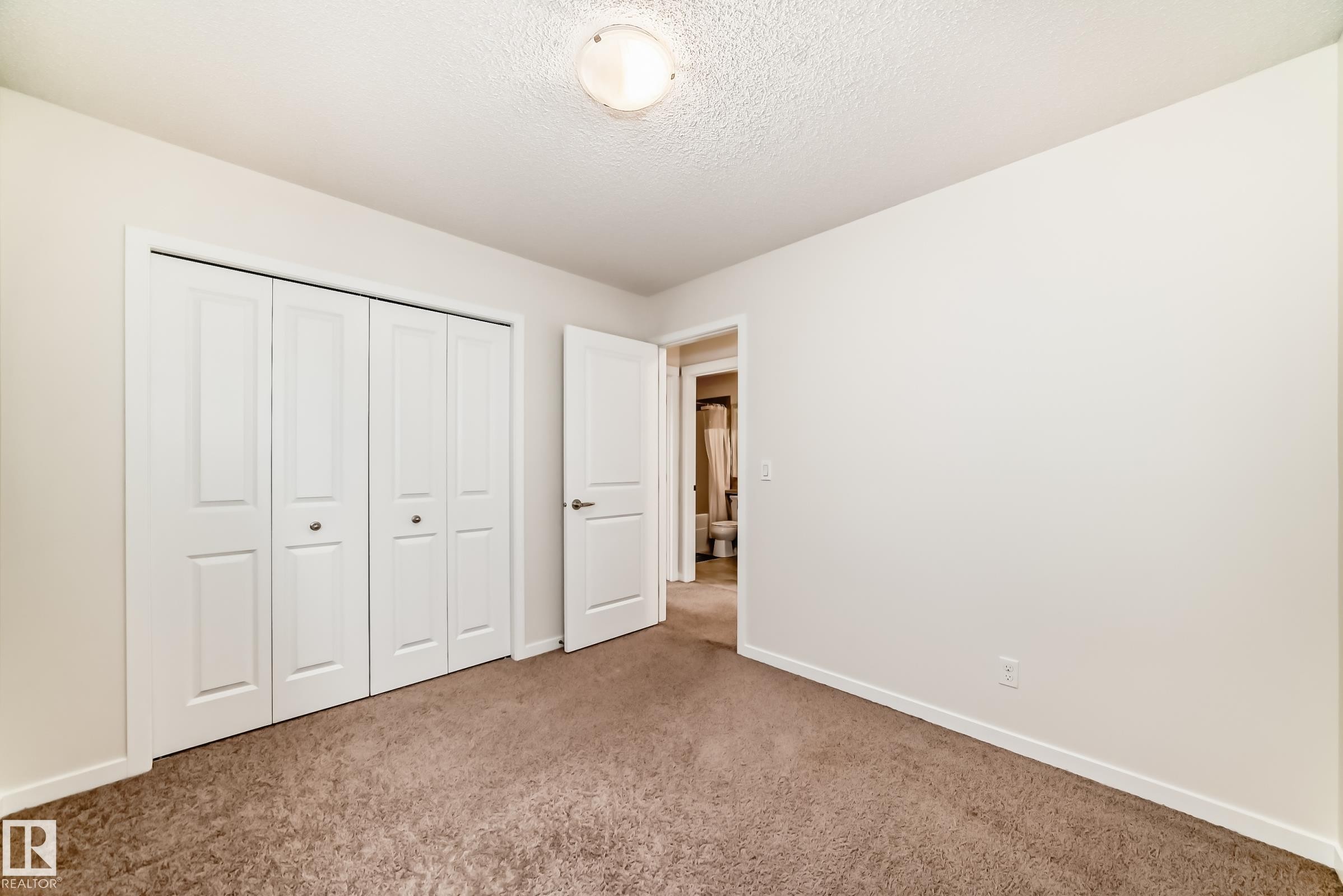 Carpeted room featuring white bi-fold closet doors, a white interior door, and a flush mount ceiling light - 18103 77 Street, Edmonton, AB