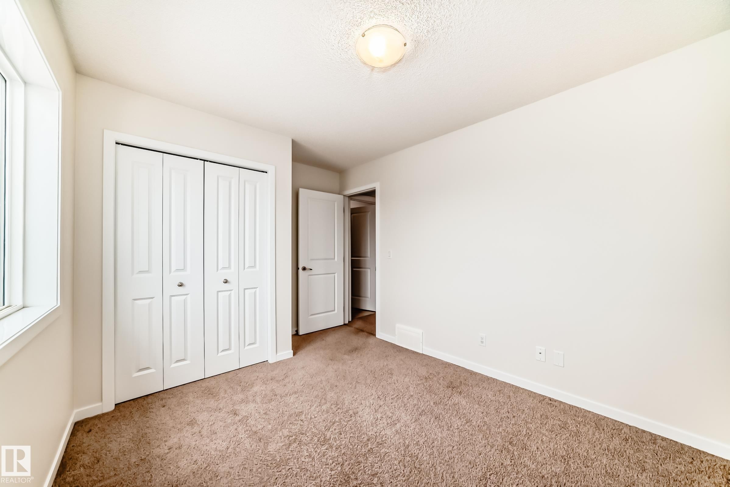 Carpeted room featuring a double bi-fold closet, a single window, and a flush-mount ceiling light fixture - 18103 77 Street, Edmonton, AB