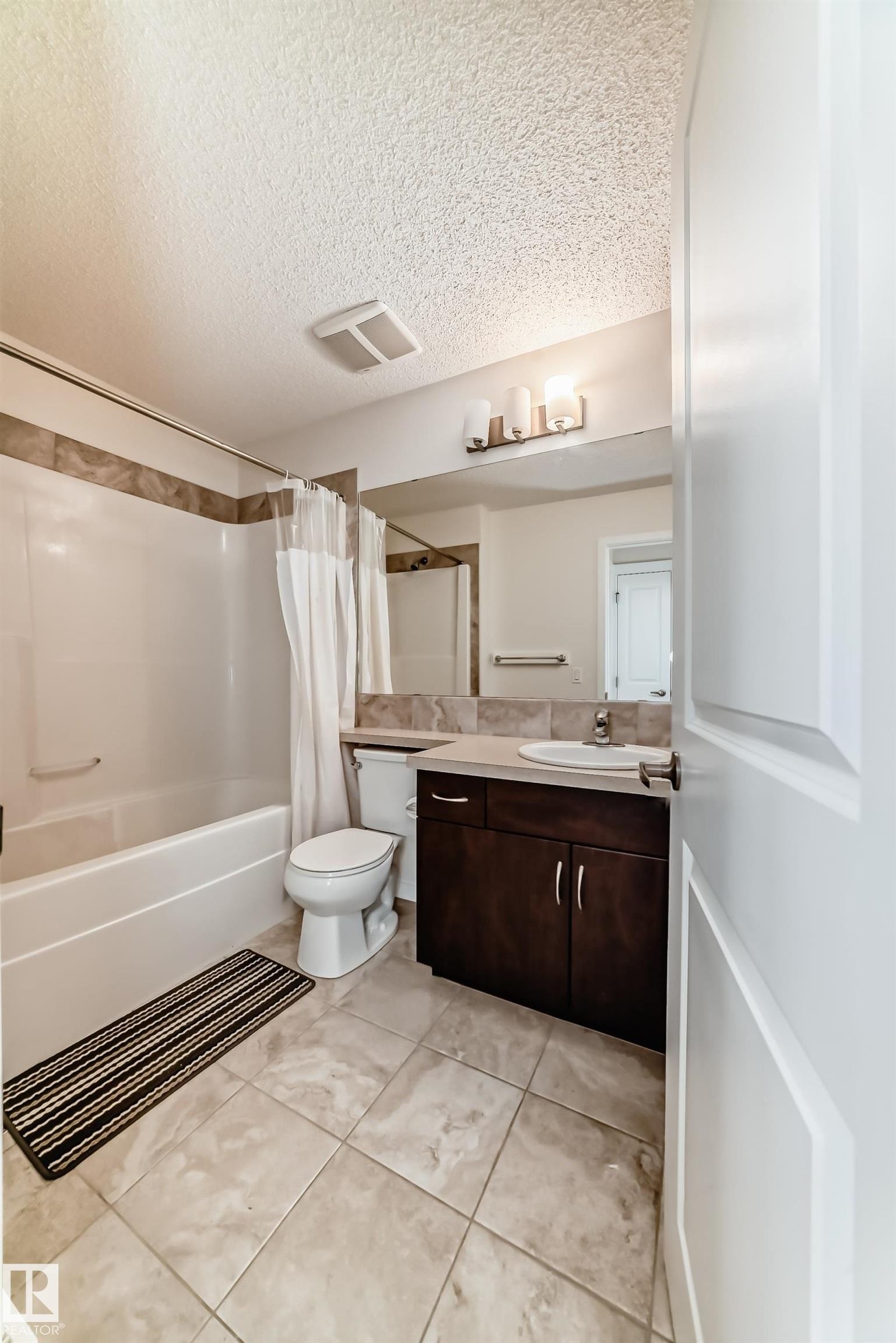 Full bathroom featuring a tub-shower combination with tile surround, a single vanity with dark wood-finish cabinetry, a white basin sink, and a large wall-mounted mirror - 18103 77 Street, Edmonton, AB