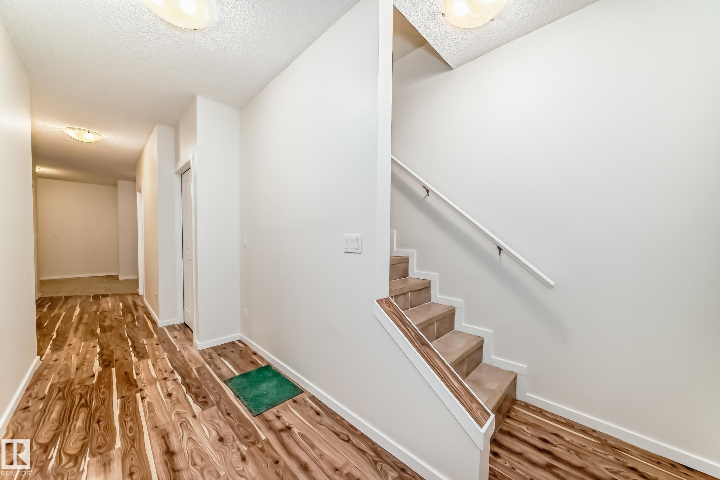 Entryway featuring wood-finish flooring and a staircase with tiled treads and a white handrail - 18103 77 Street, Edmonton, AB