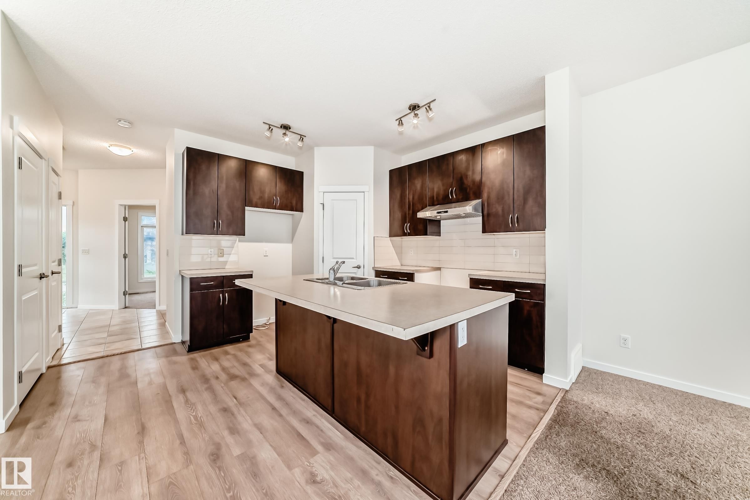 Kitchen featuring an expansive center island with light-toned countertops, dark wood-finish cabinetry, subway tile backsplash, and light wood-finish flooring - 18103 77 Street, Edmonton, AB